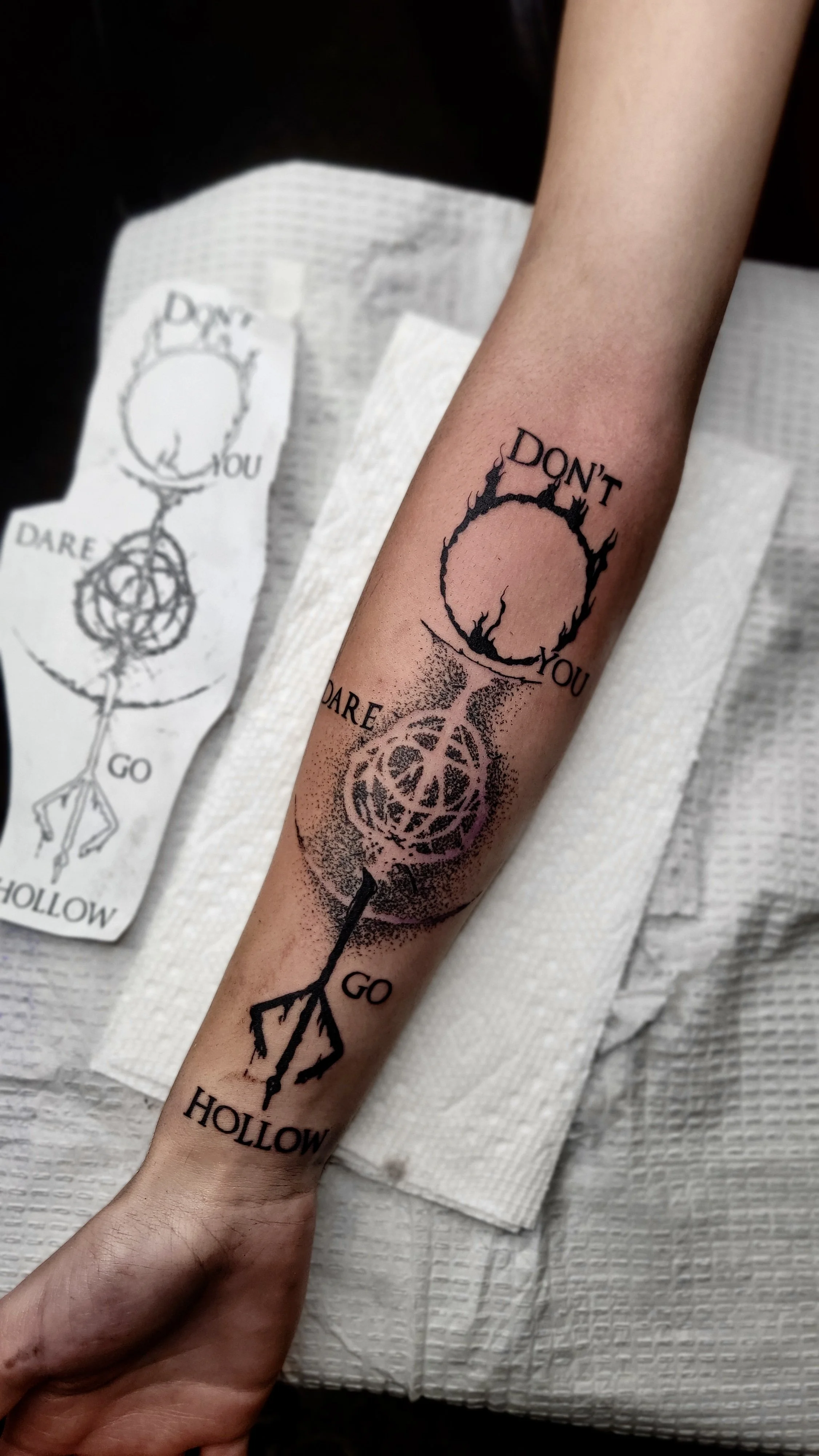 Tattoo on person's forearm with a minimalist tree and an arrow. The tree has a circular, jagged outline with black ink. The tattoo includes the text 'DON'T YOU DARE GO HOLLOW' surrounding the circle.