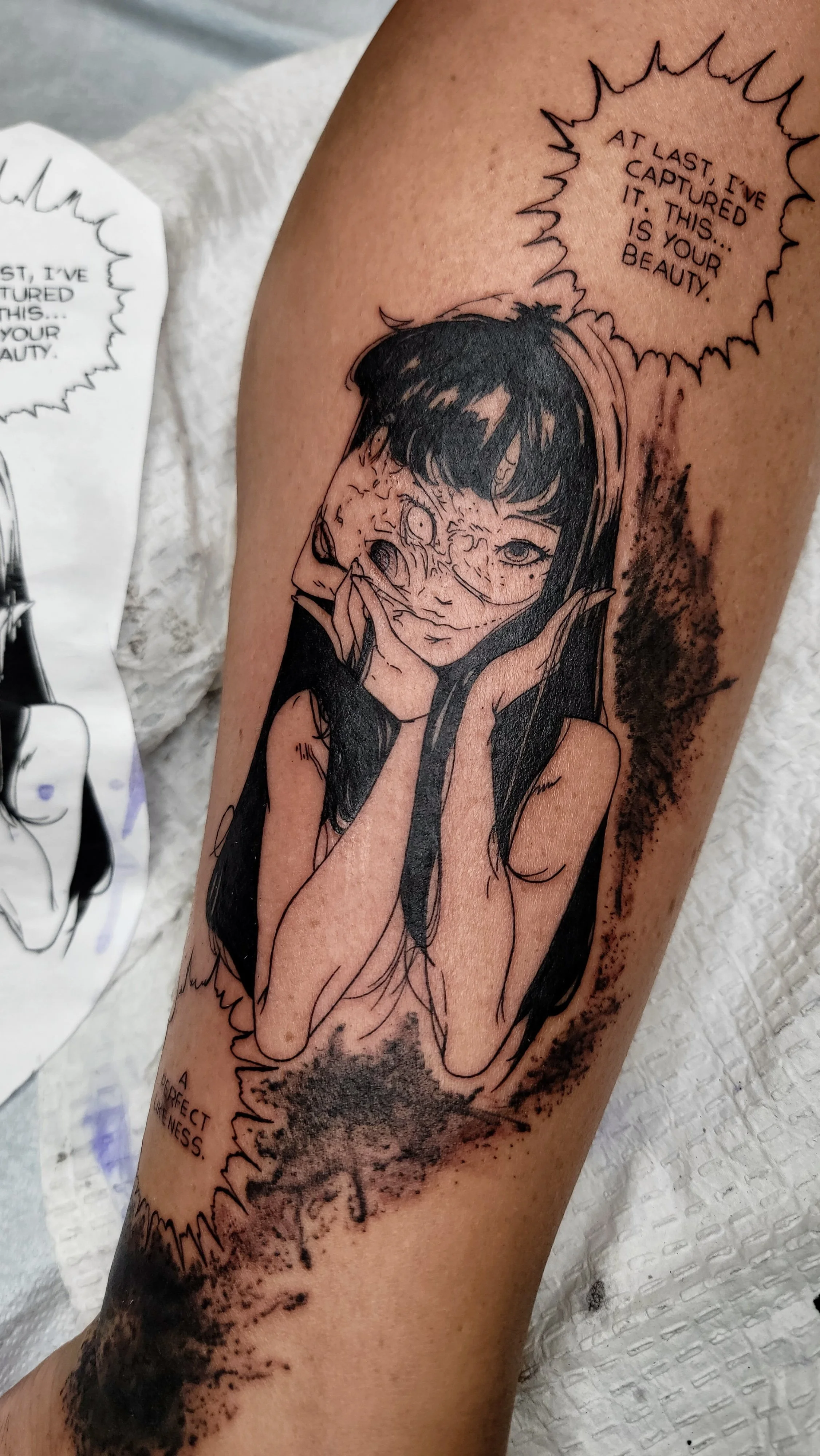 Tattoo of a girl with long dark hair, resting her chin on her hands, with a speech bubble that reads, 'At last, I've captured this... It is your beauty.'