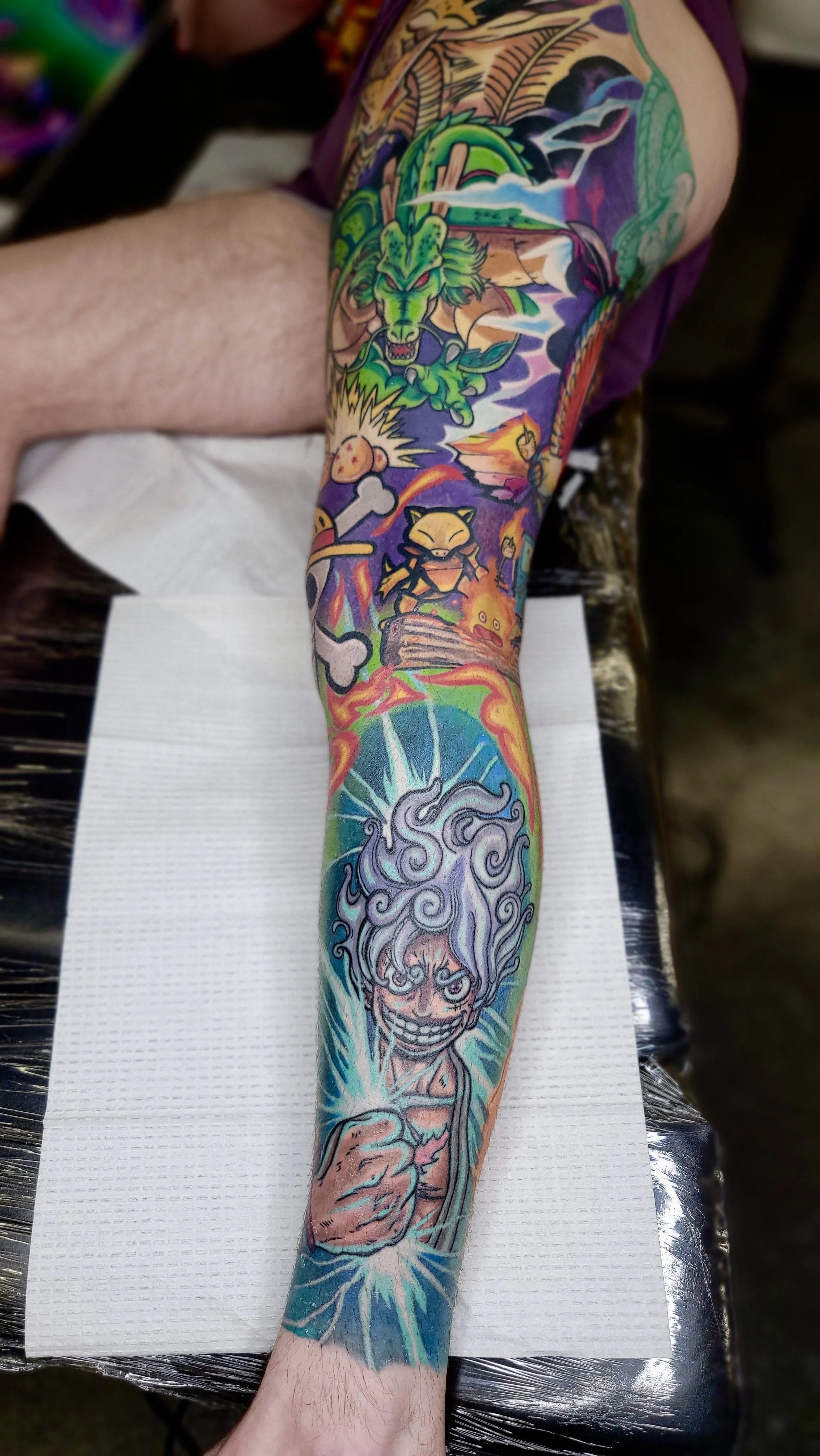 Colorful tattoo sleeve featuring a fierce green dragon, characters from video games, and a detailed depiction of a lightning-powered figure with swirling clouds, all in vibrant hues.