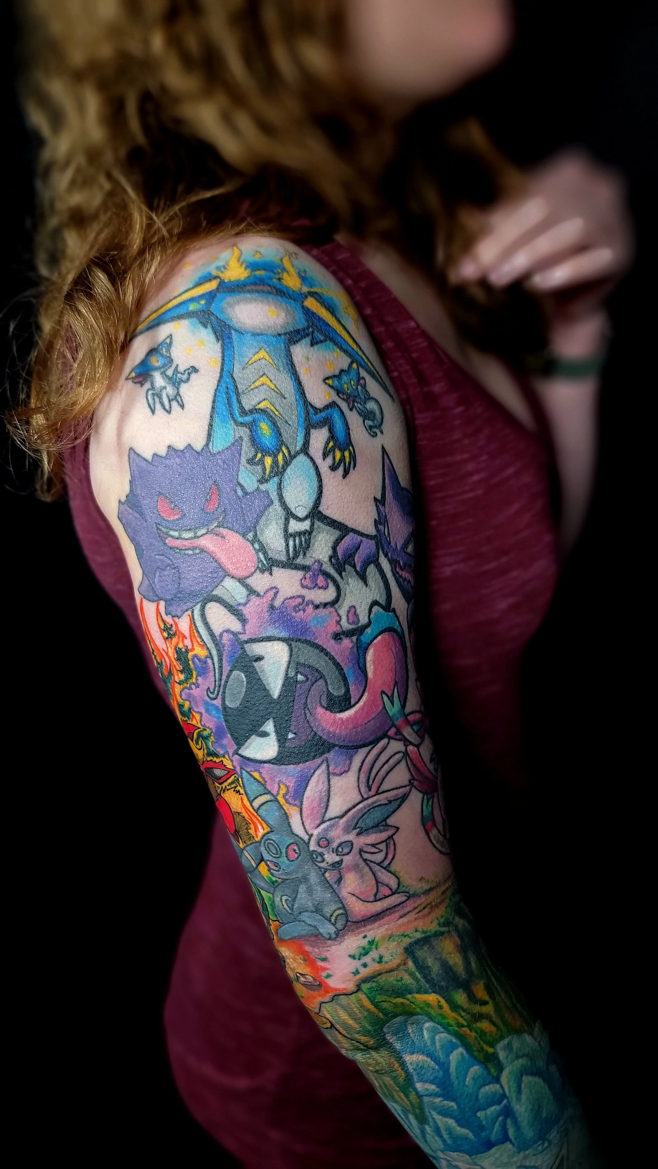 Close-up of a person’s arm with colorful Pokémon-themed tattoo artwork featuring various Pokémon characters and elements, with a small portion of the person's face and hand visible.
