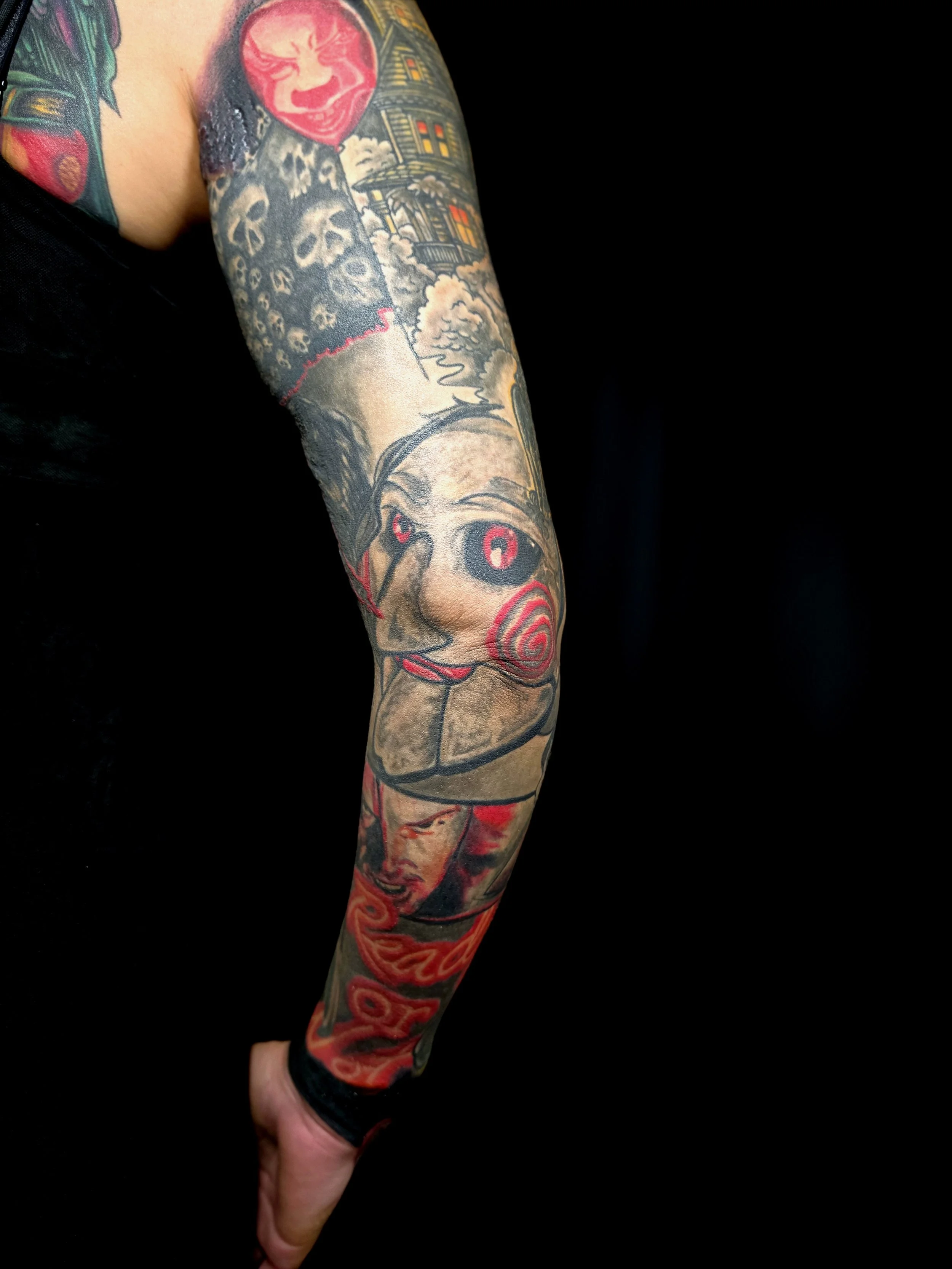 Colorful full arm tattoo featuring a clown face, a spooky house, and a skeleton.
