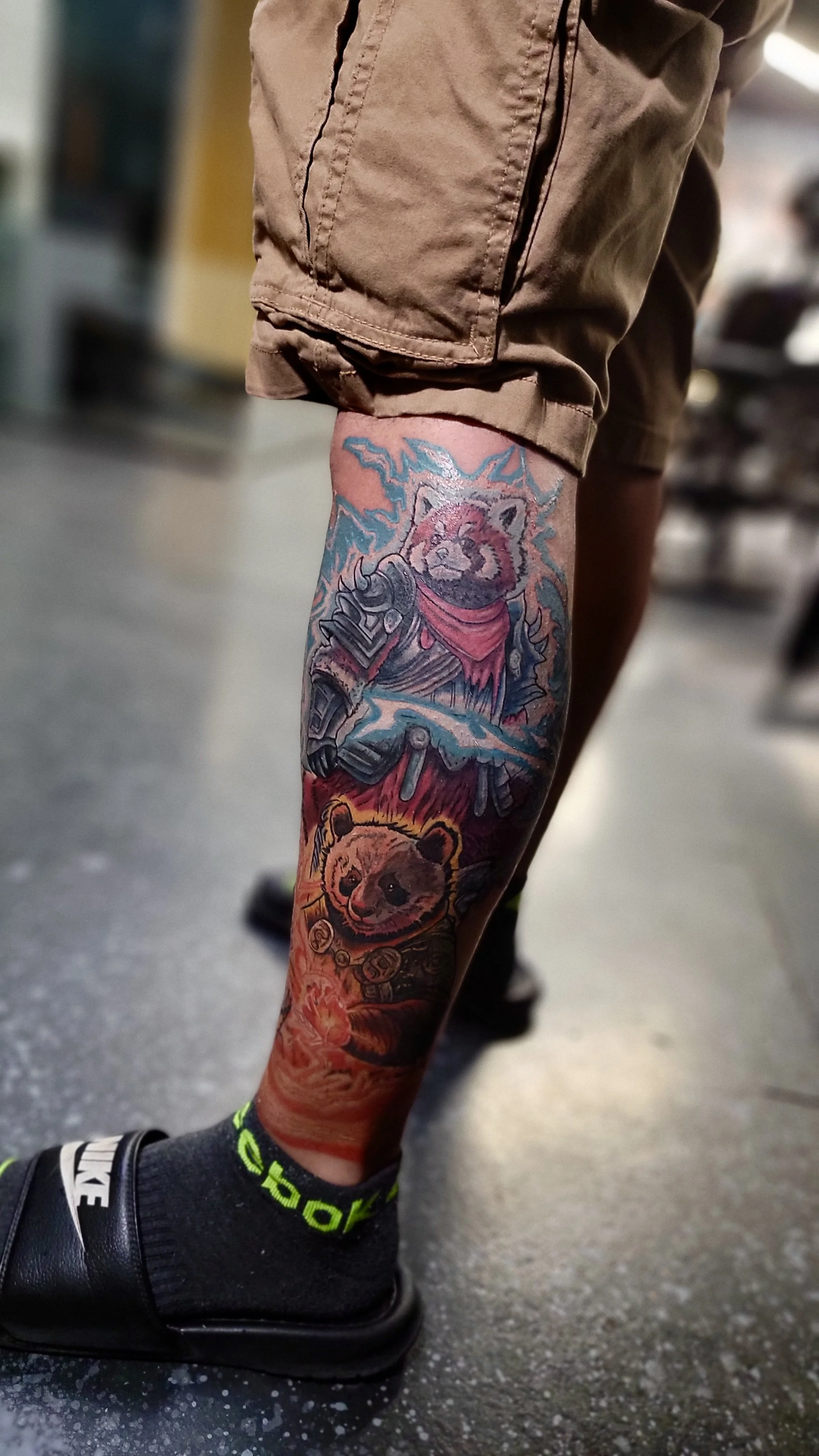 Colorful tattoo sleeve on a person's leg, featuring a cat with lightning, a bear, and various other designs, wearing a red cape and armor.
