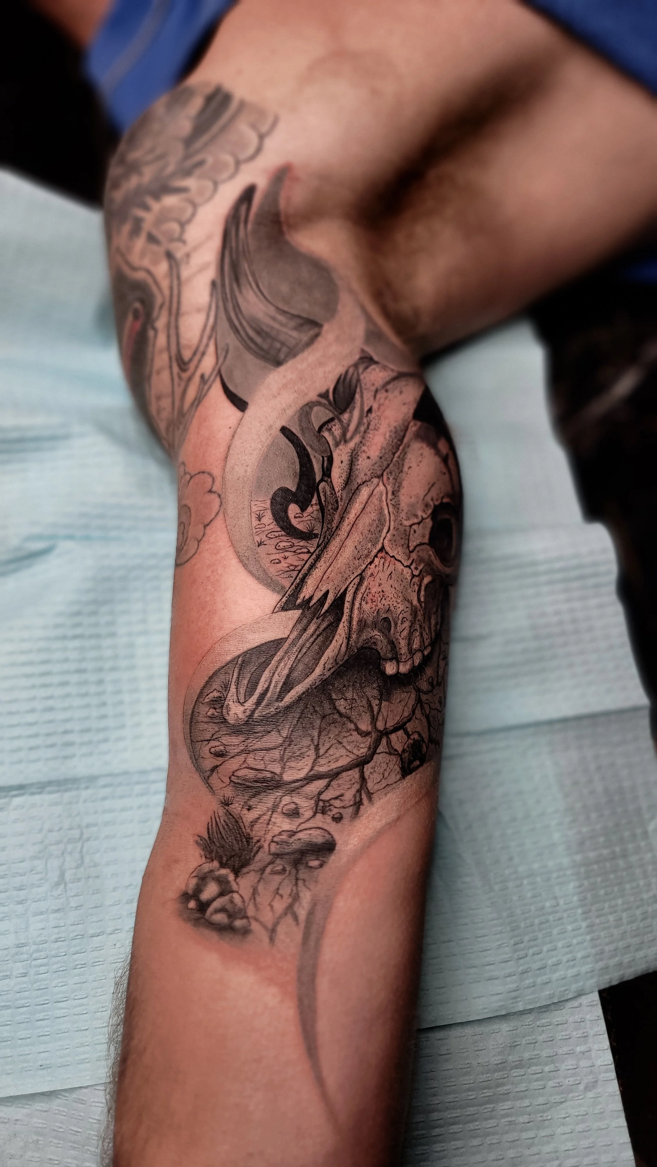 Close-up of a forearm tattoo featuring a detailed skull, a moon, and abstract line art.