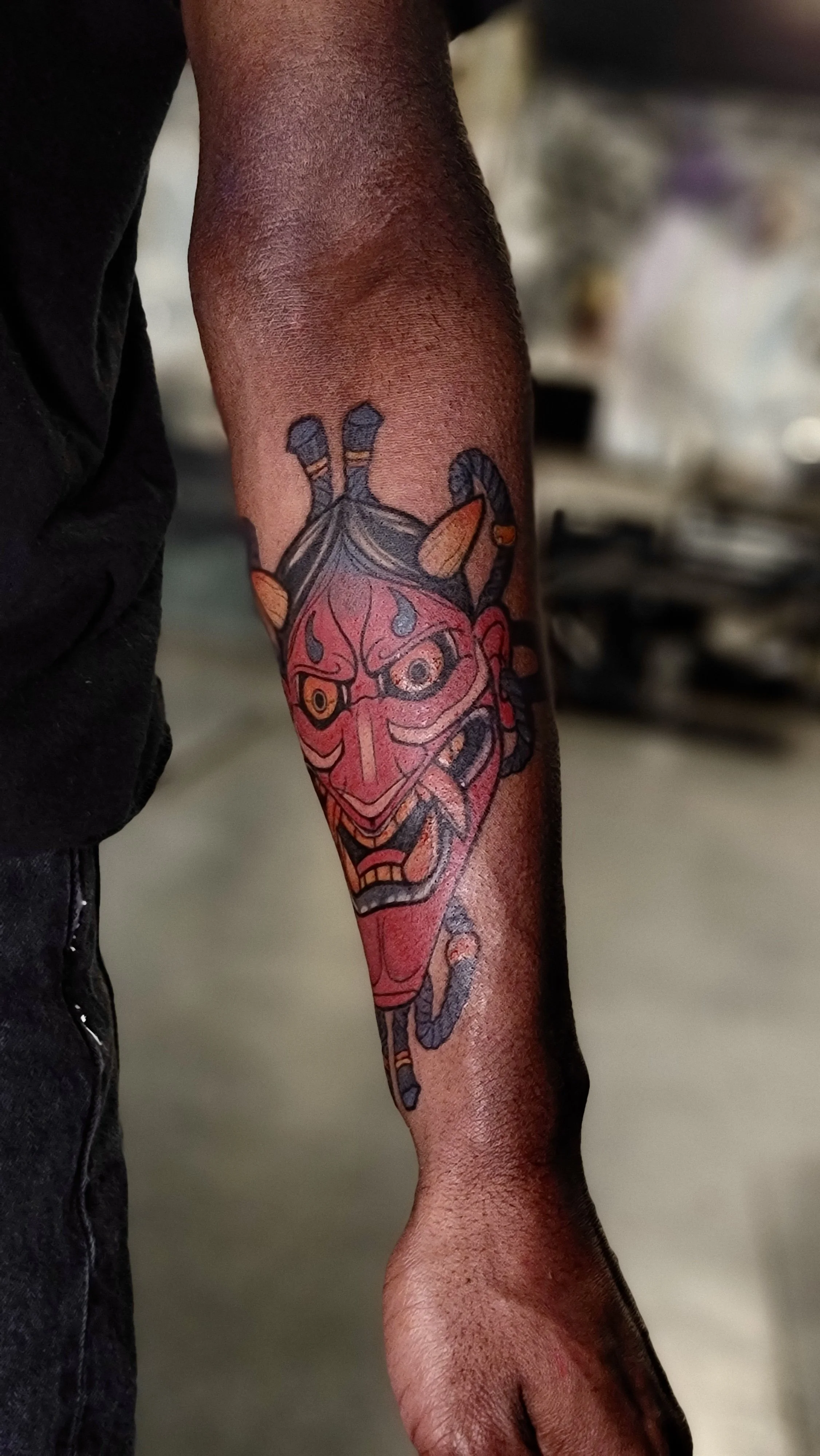 Tattoo of a traditional Japanese Hannya mask on a person's forearm.