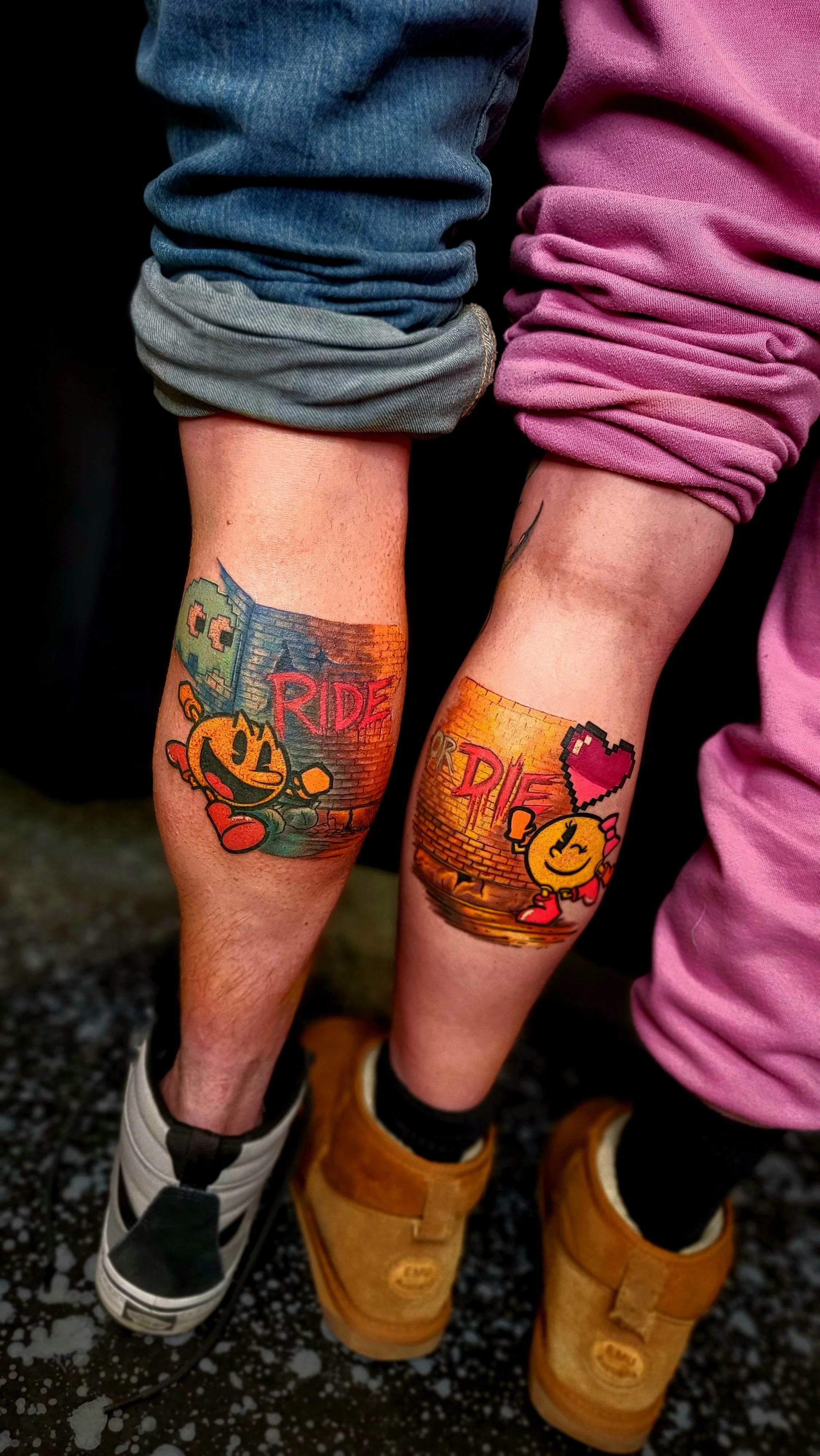 Two people with tattoos on their calves, featuring cartoon characters and the word 'RIDE' in colorful letters, wearing sneakers and boots.