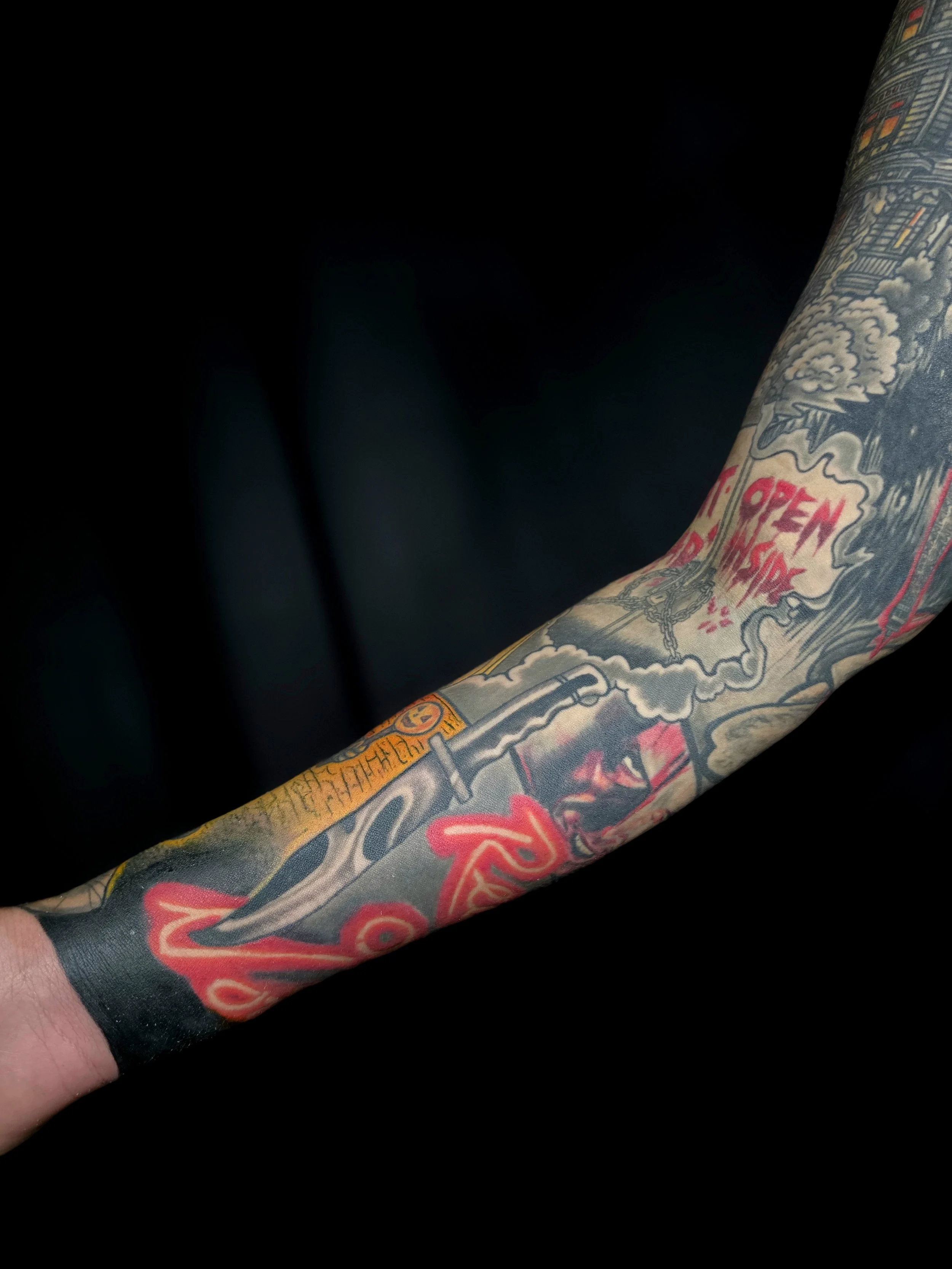 Close-up of a tattooed arm with colorful illustrations and text, against a dark background.
