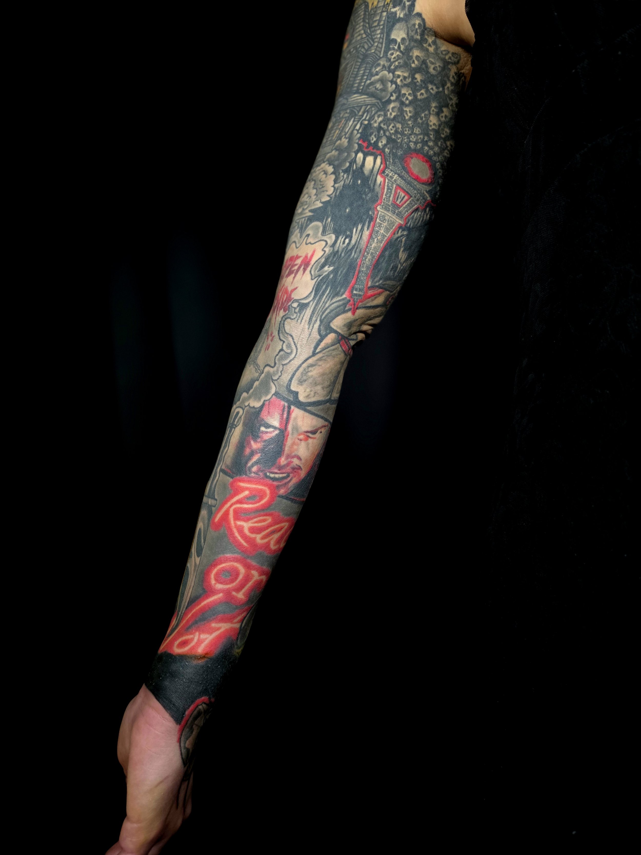 Close-up of a person's arm and hand showing colorful tattoos, against a black background.
