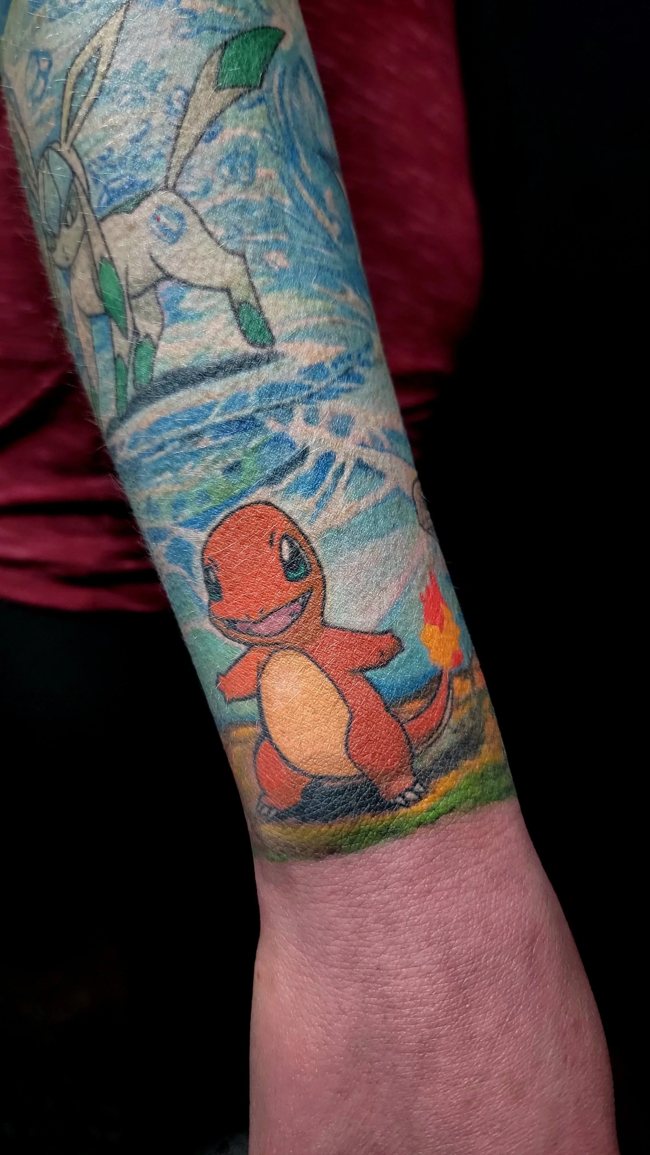 A tattoo of Charmander, a Pokémon character, holding a small flame, with a background featuring water, trees, and a sky.