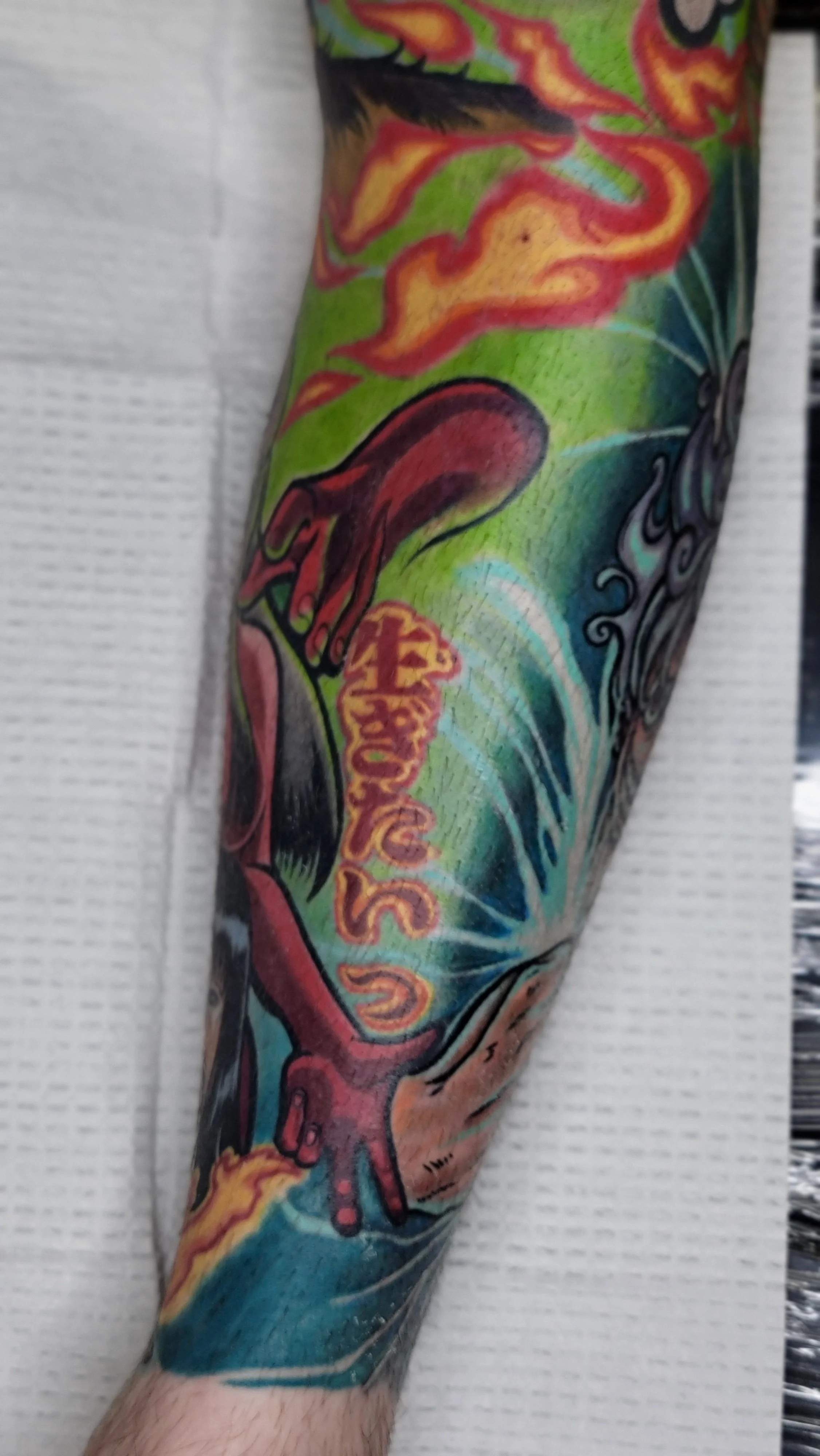 Colorful tattoo sleeve featuring a red and orange dragon, a yellow flower, and swirling blue and green patterns.
