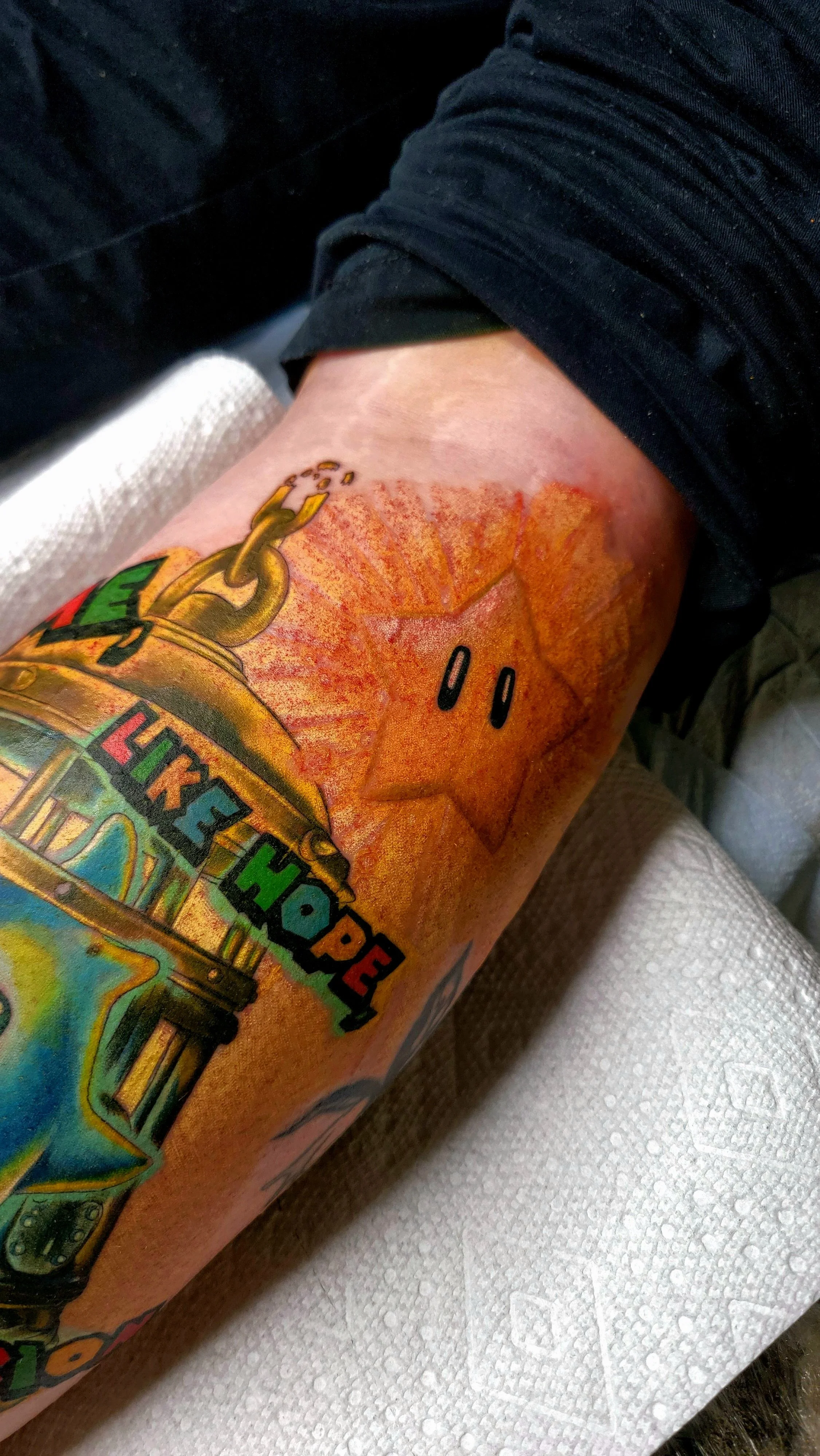 Colorful tattoo on person's arm featuring a vintage jukebox with rainbow colors and a cartoon face with a wide smile.