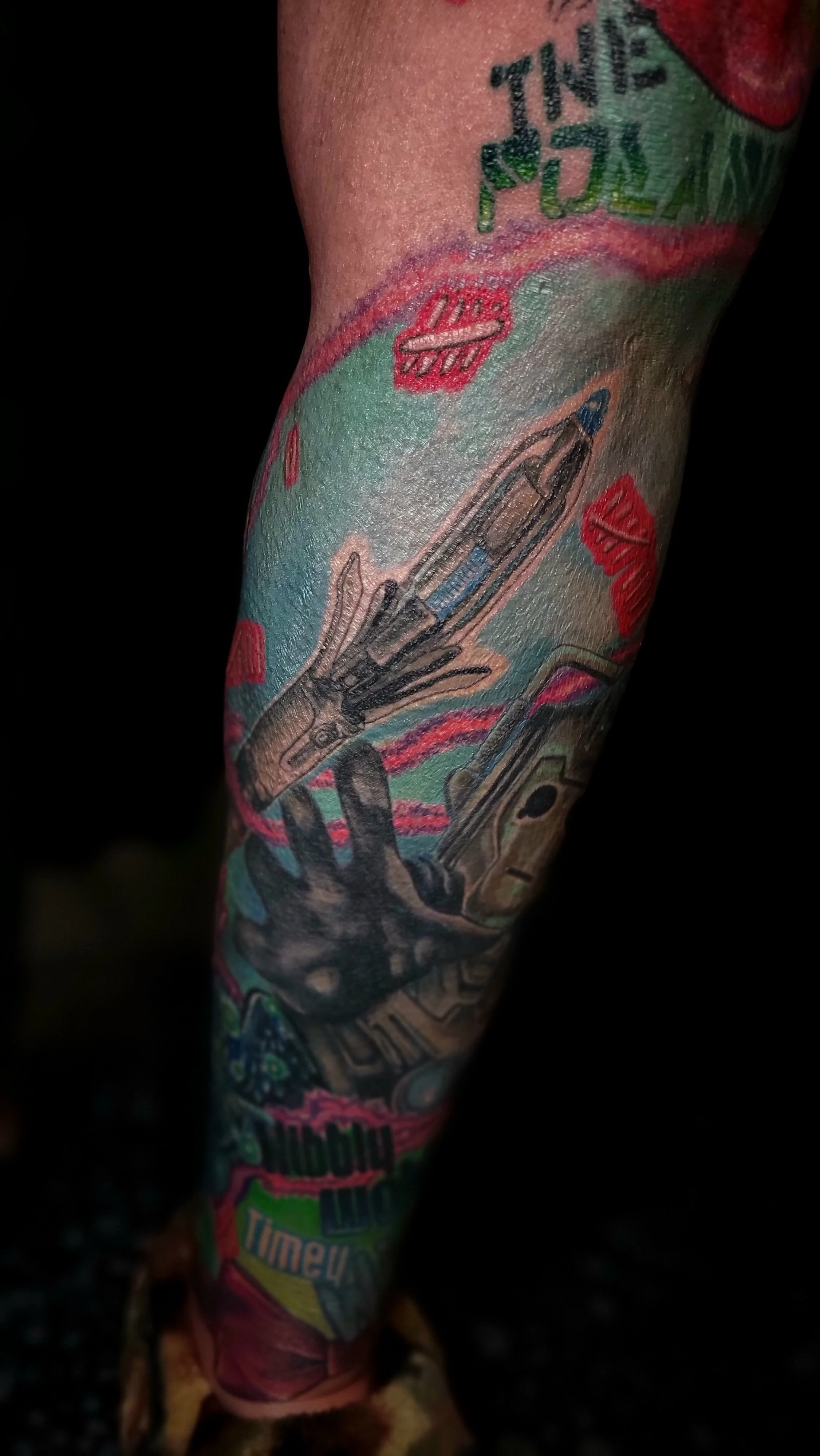 Close-up of a tattooed arm featuring colorful comic-style illustrations of a handgun, faces, and text in bold, vibrant colors.