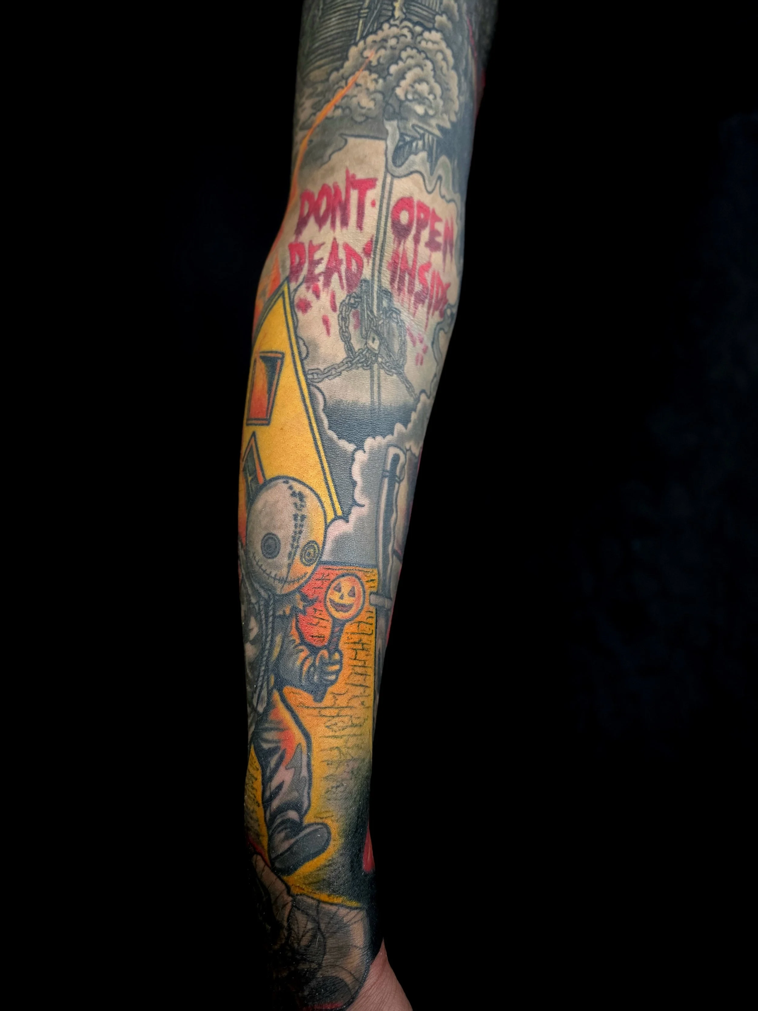 Tattoo on arm featuring a skeleton holding a sign that says "Point of No Return." The tattoo includes clouds, chains, and various colorful designs.