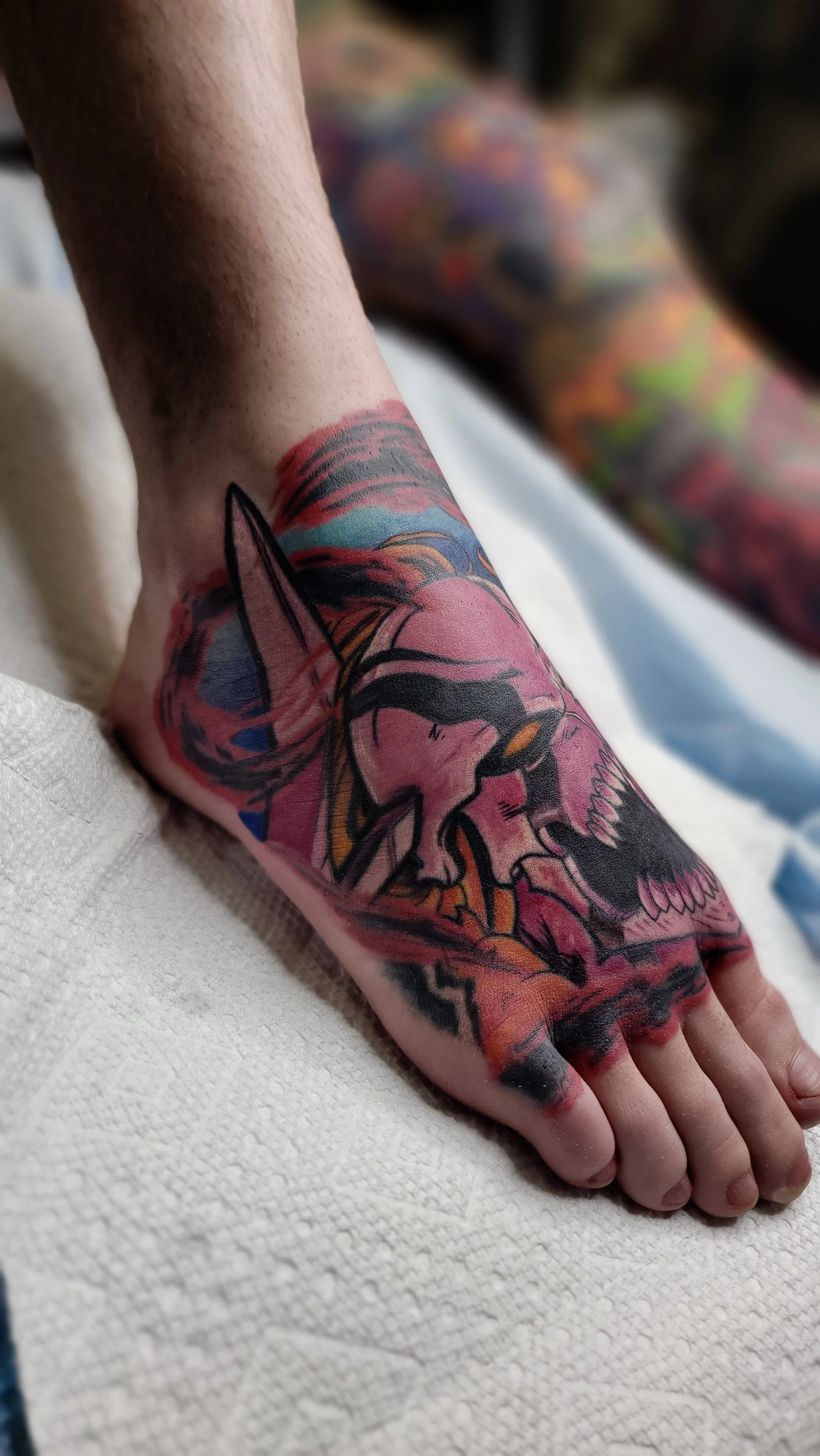 Colorful tattoo of a fox with a skull on a person's arm, with a background of vibrant colors.