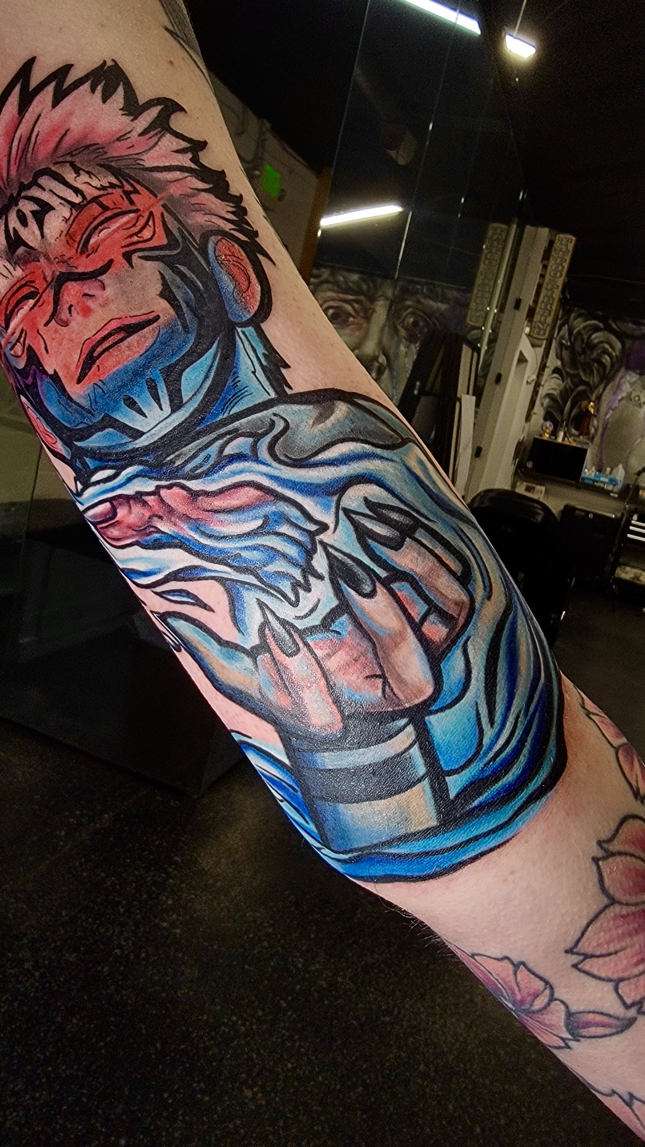 Colorful tattoo of a dragon on a person's arm, featuring red, blue, black, and beige colors in a stylized design.
