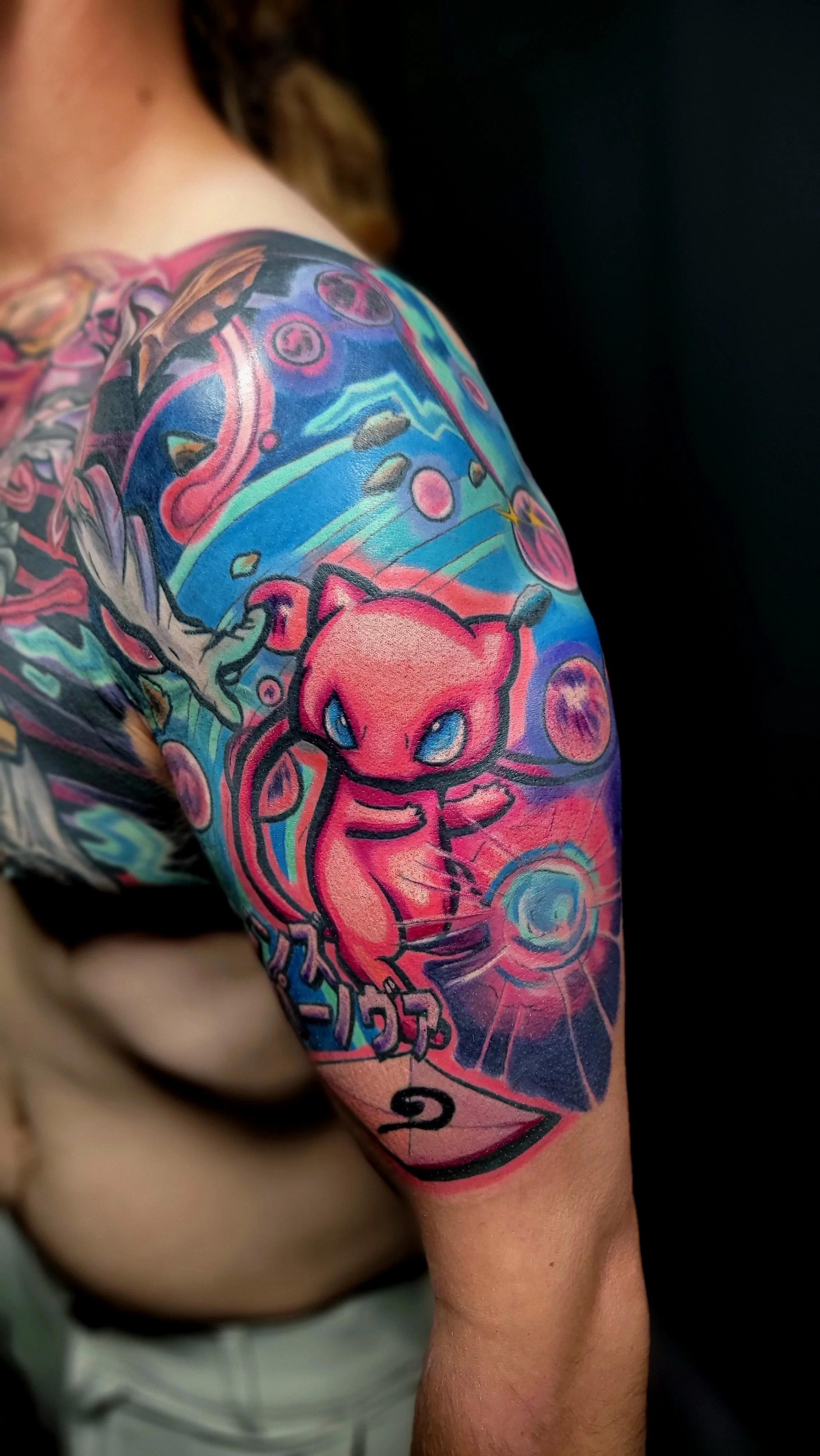 Colorful tattoo sleeve featuring a pink creature with blue eyes, surrounded by abstract designs and vibrant colors.