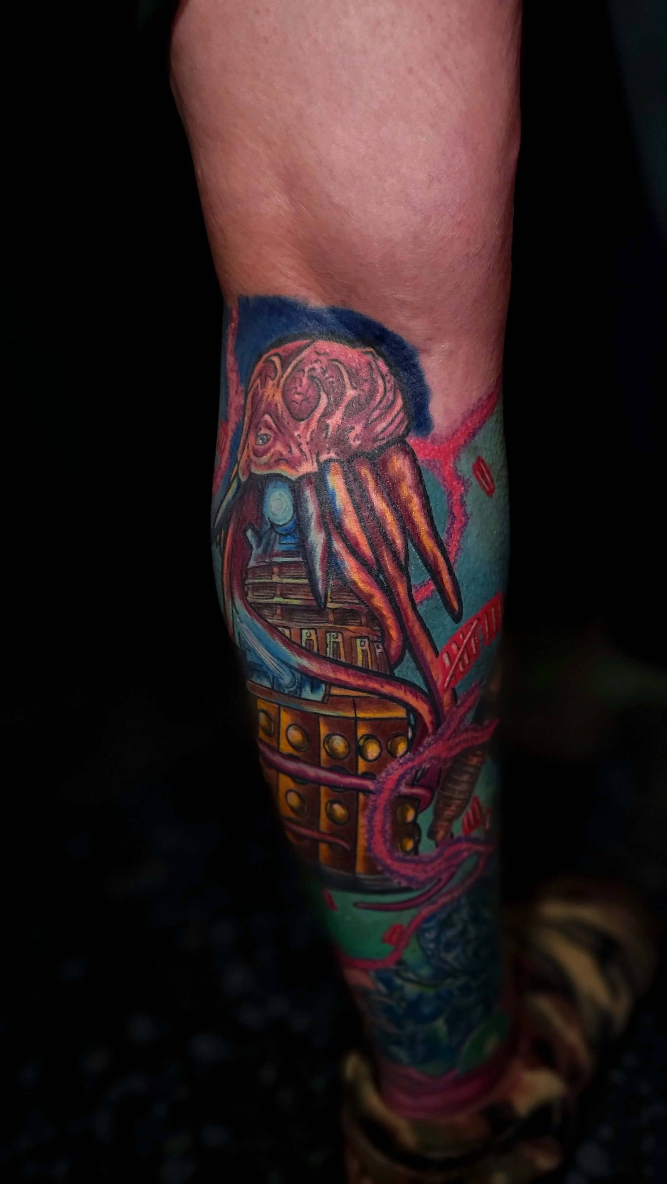 Close-up of a person's arm with a colorful tattoo featuring an abstract design with various shapes and vibrant colors.