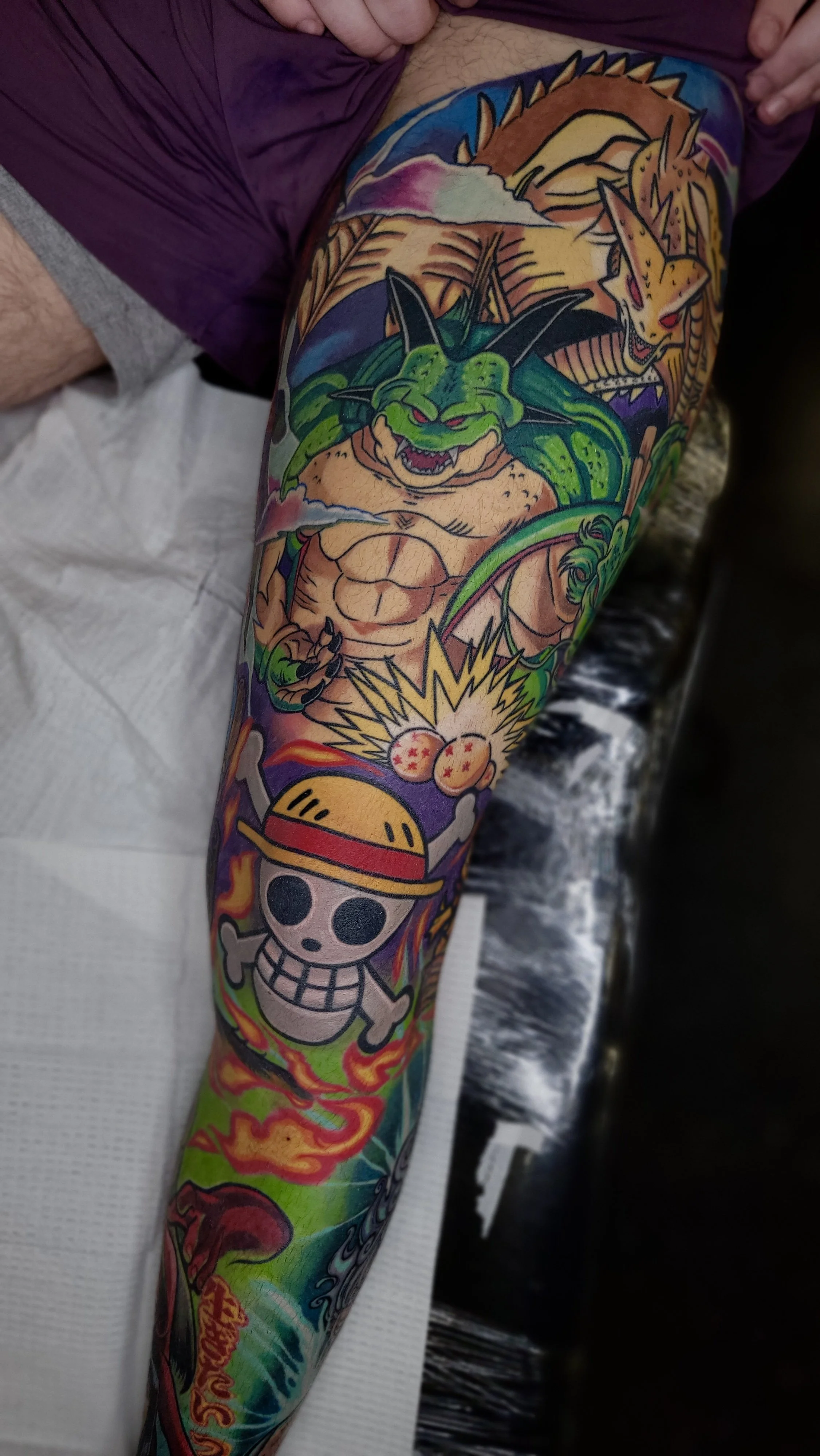 Colorful tattoo sleeve featuring anime and cartoon characters, including a green muscular creature, a skull with a straw hat, and a fierce fox with multiple tails, surrounded by flames and vibrant backgrounds.