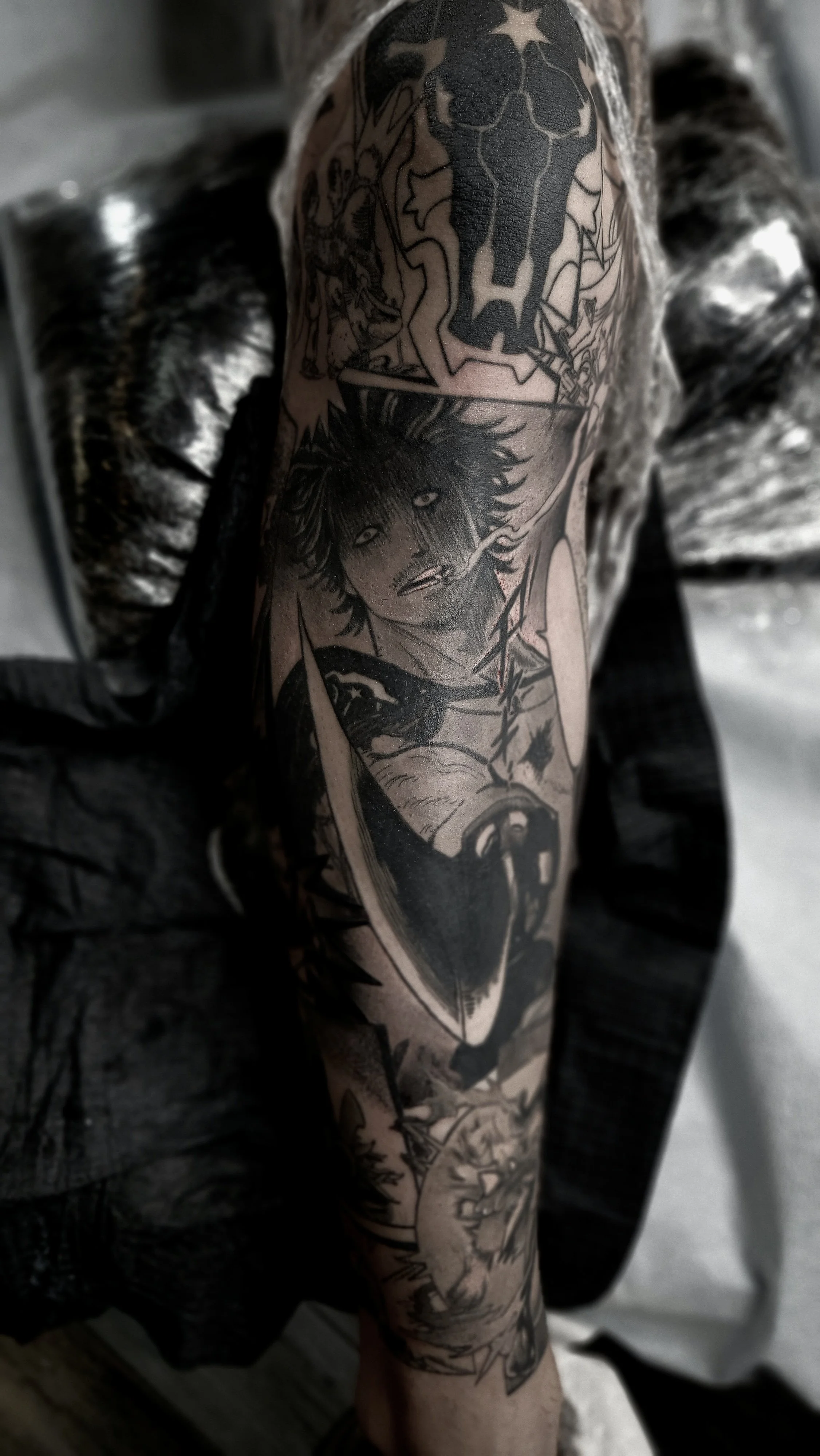 Close-up of a person's arm with a black ink tattoo featuring a detailed wolf face, a woman, and various abstract designs.