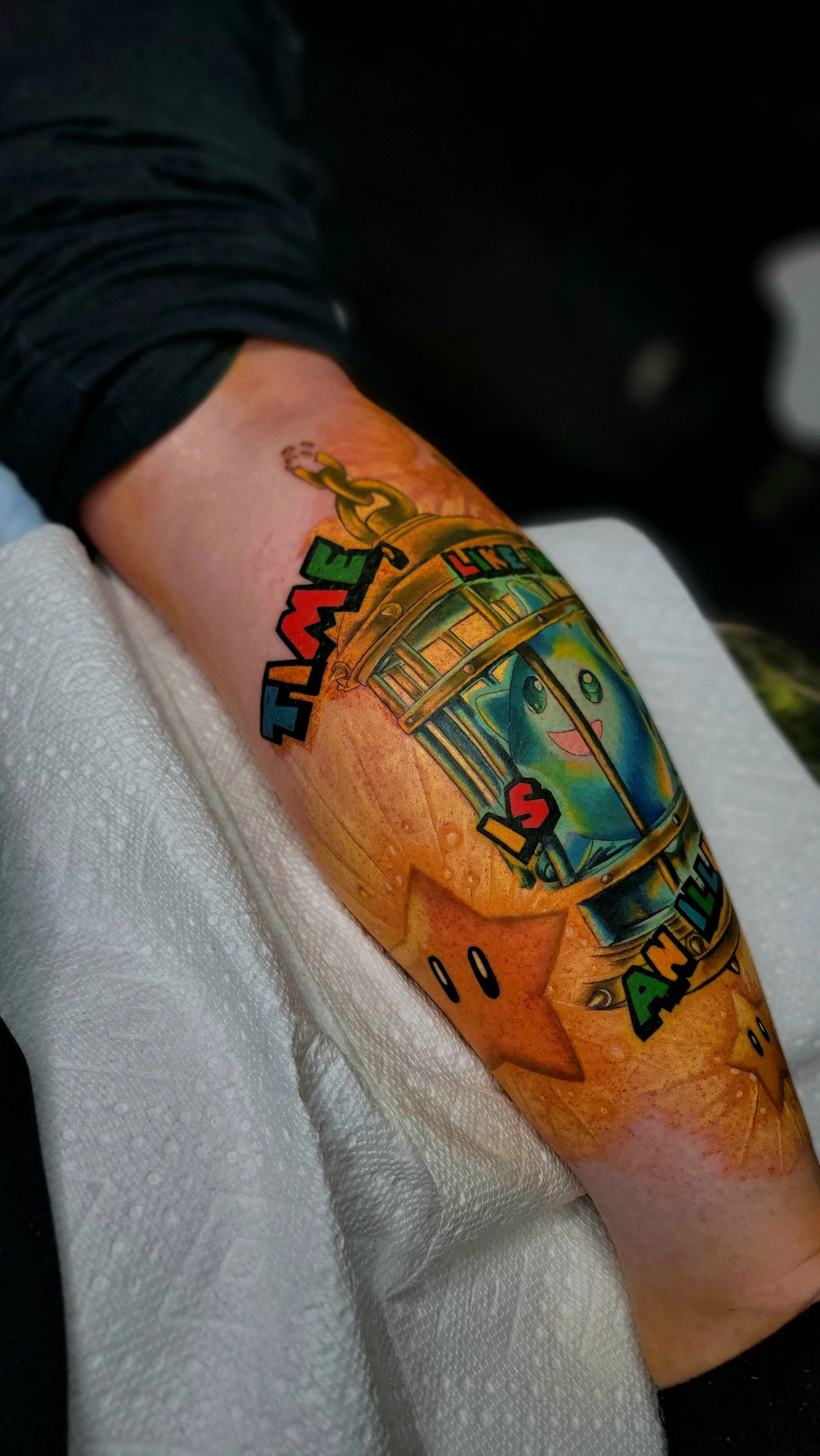 Colorful tattoo of a cartoon ghost inside a pumpkin, with rainbow-colored text, on person's arm.
