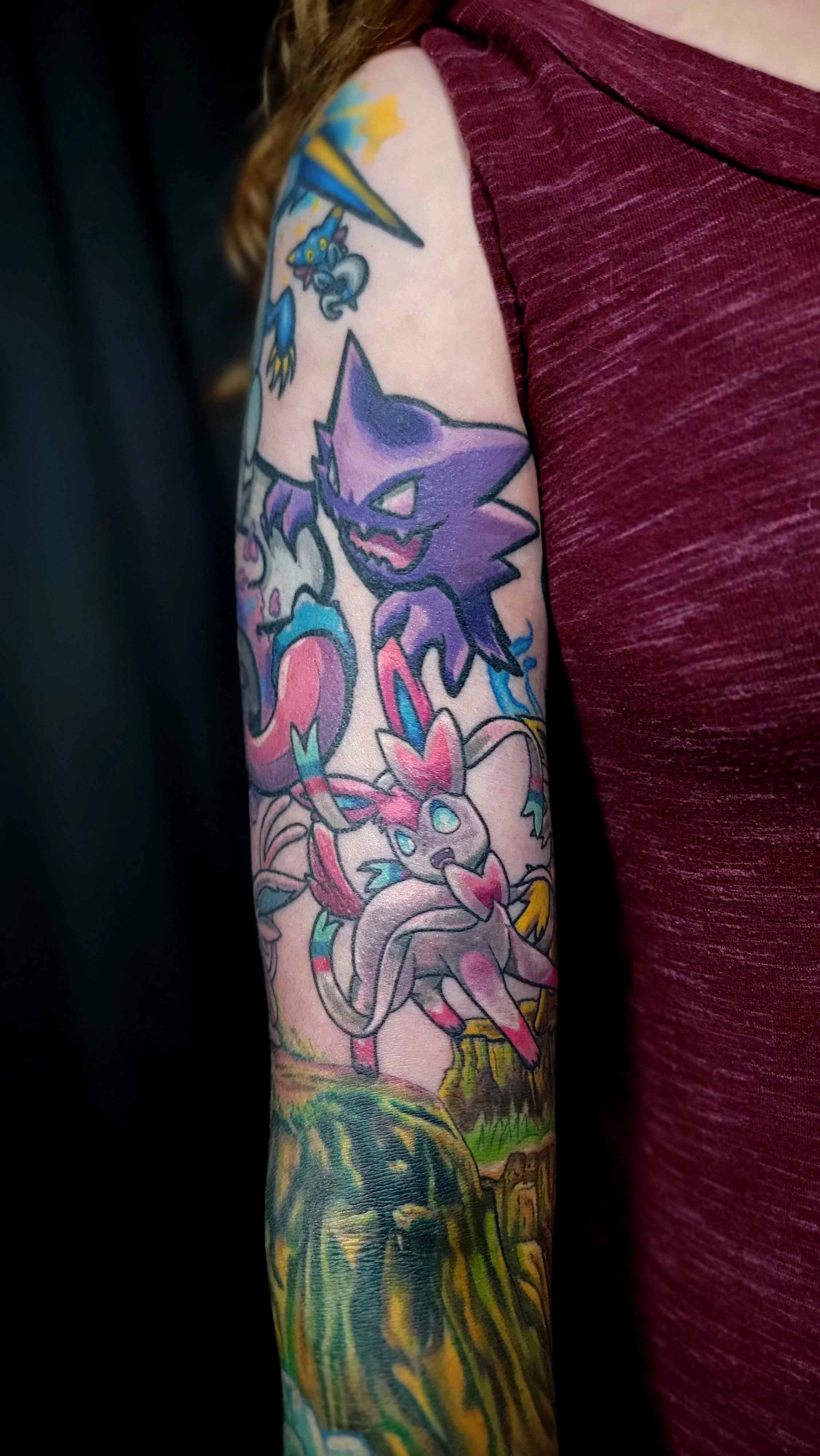 Colorful tattoo sleeve with various designs including a purple bat-like creature, a pink and gray squirrel, and other mythical and whimsical elements on a person's arm.