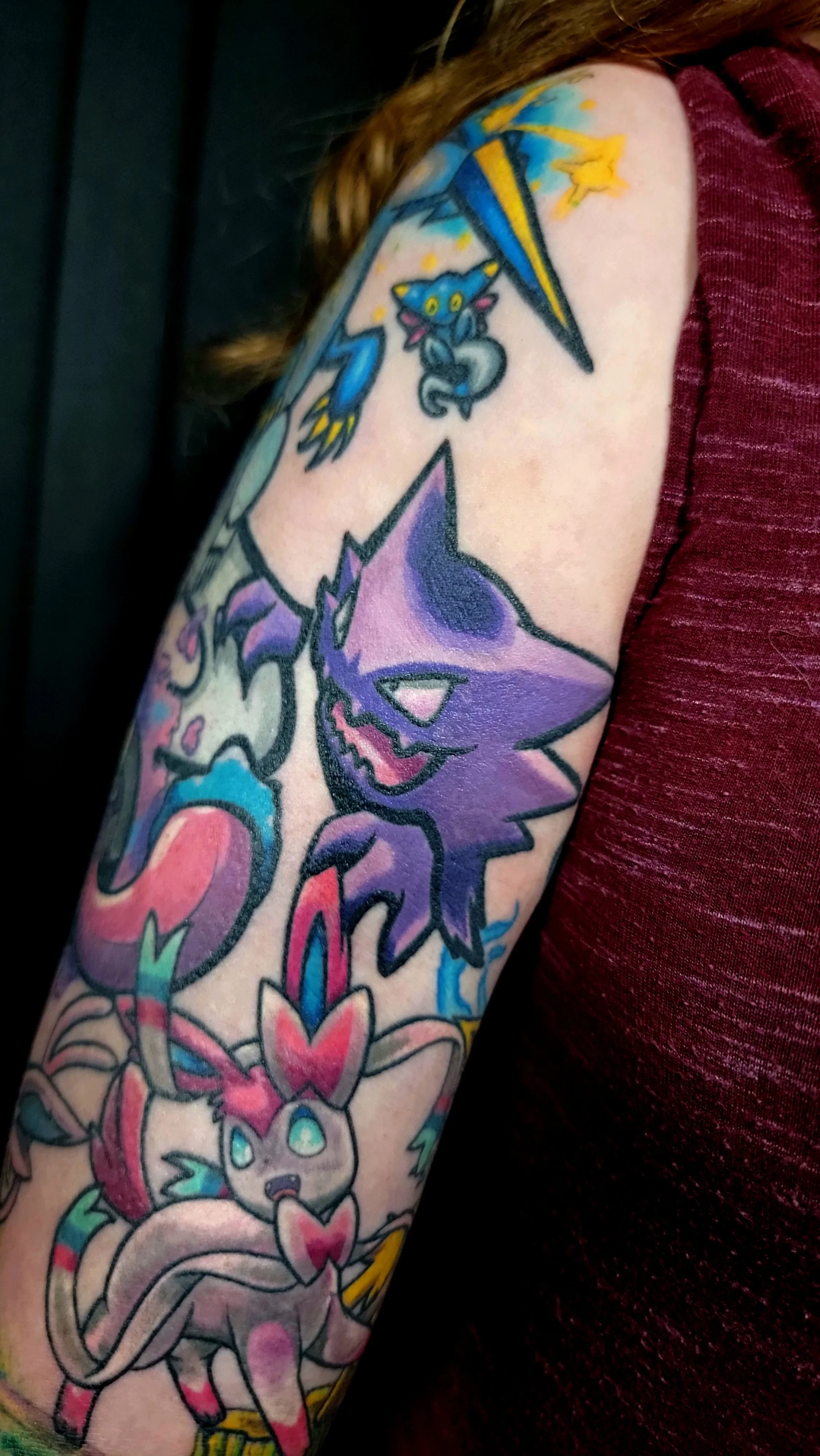 Tattoo of a purple and pink fox with a mischievous expression and a small creature with large eyes and a smiling face, surrounded by colorful abstract designs.