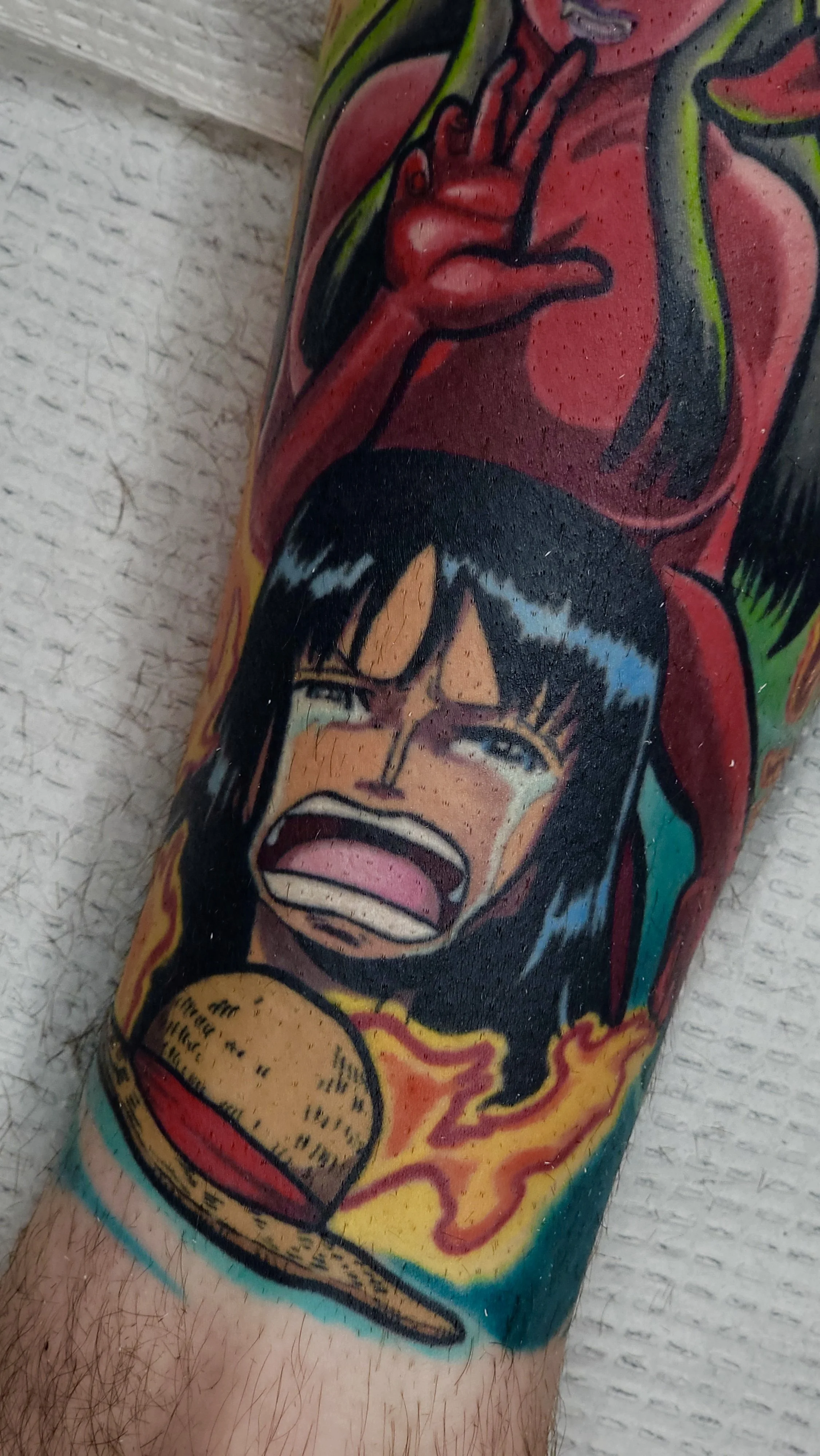 A tattoo on a person's arm depicts a screaming woman with black hair, hugging a large burger with visible buns, lettuce, and cheese, surrounded by flames and vibrant colors.