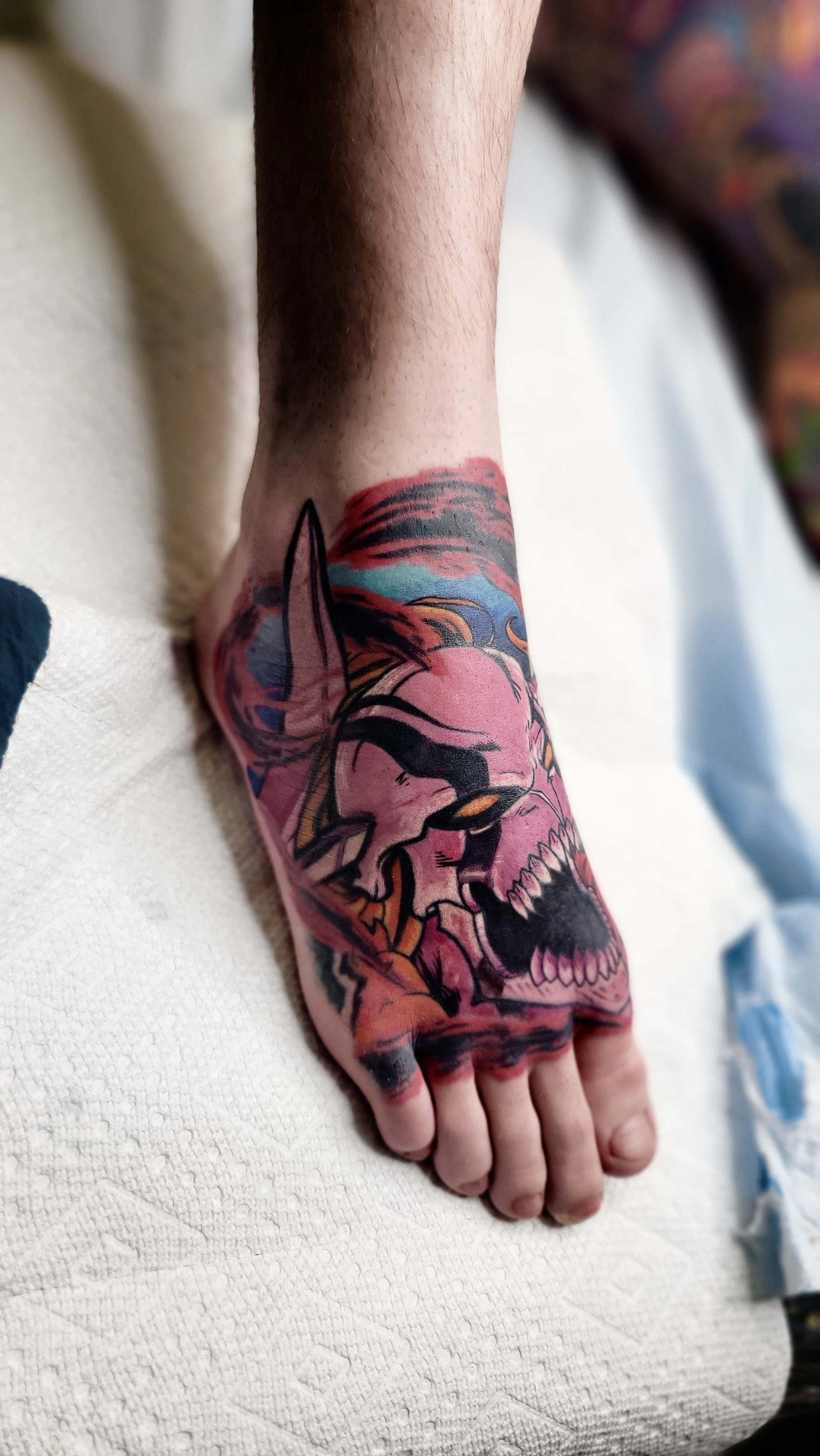 Close-up of a person's arm with a colorful tattoo of a skull, a fox, and a sunset scene.