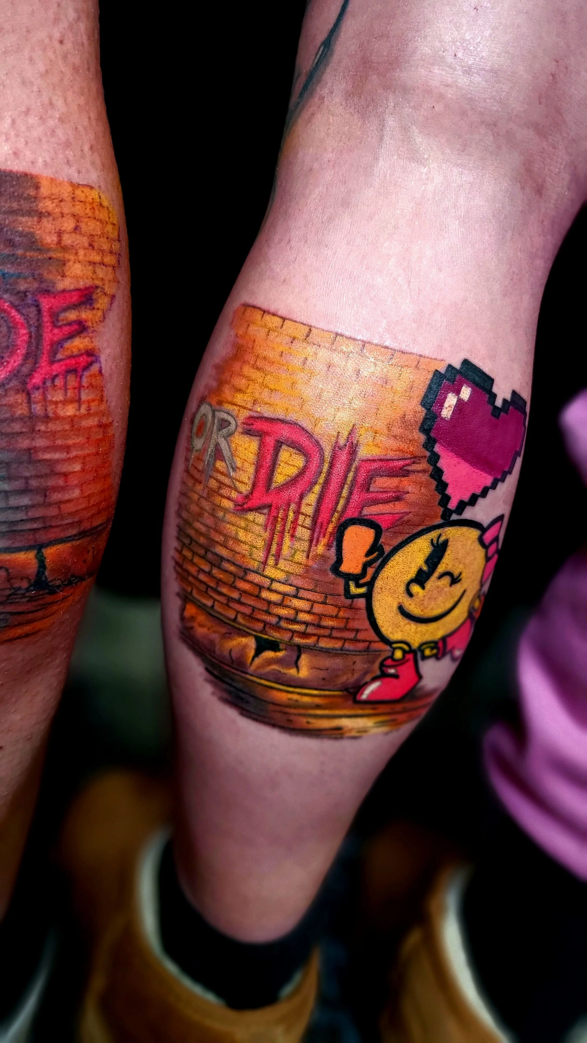Colorful tattoo on person's arm featuring a smiling yellow cartoon character with red boots, holding a pizza slice, with brick wall and graffiti art in the background.