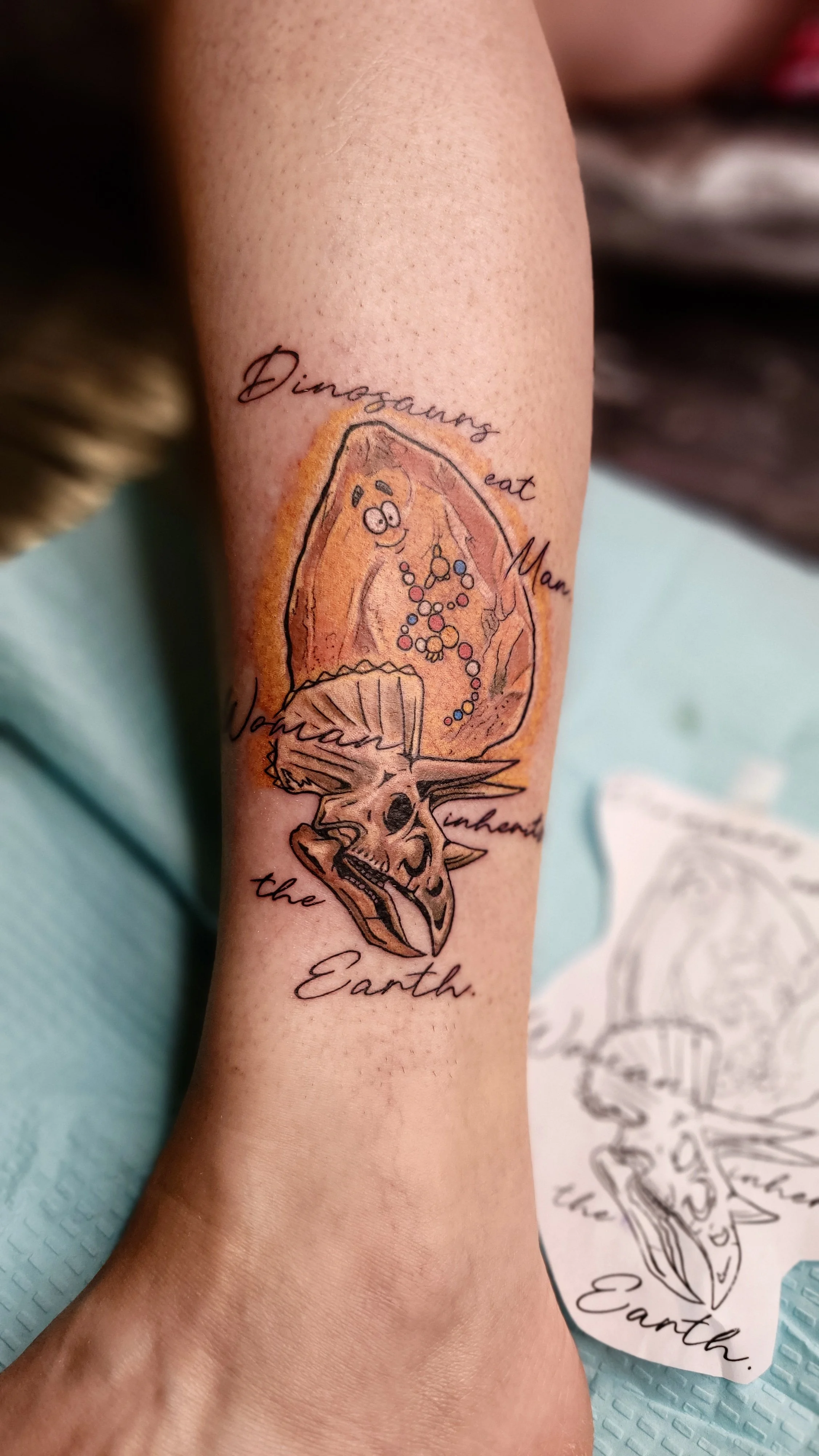 Tattoo of a dinosaur skeleton with a colorful chart on its body, surrounded by the words 'Dinosaur eat Mom the Earth' in cursive.