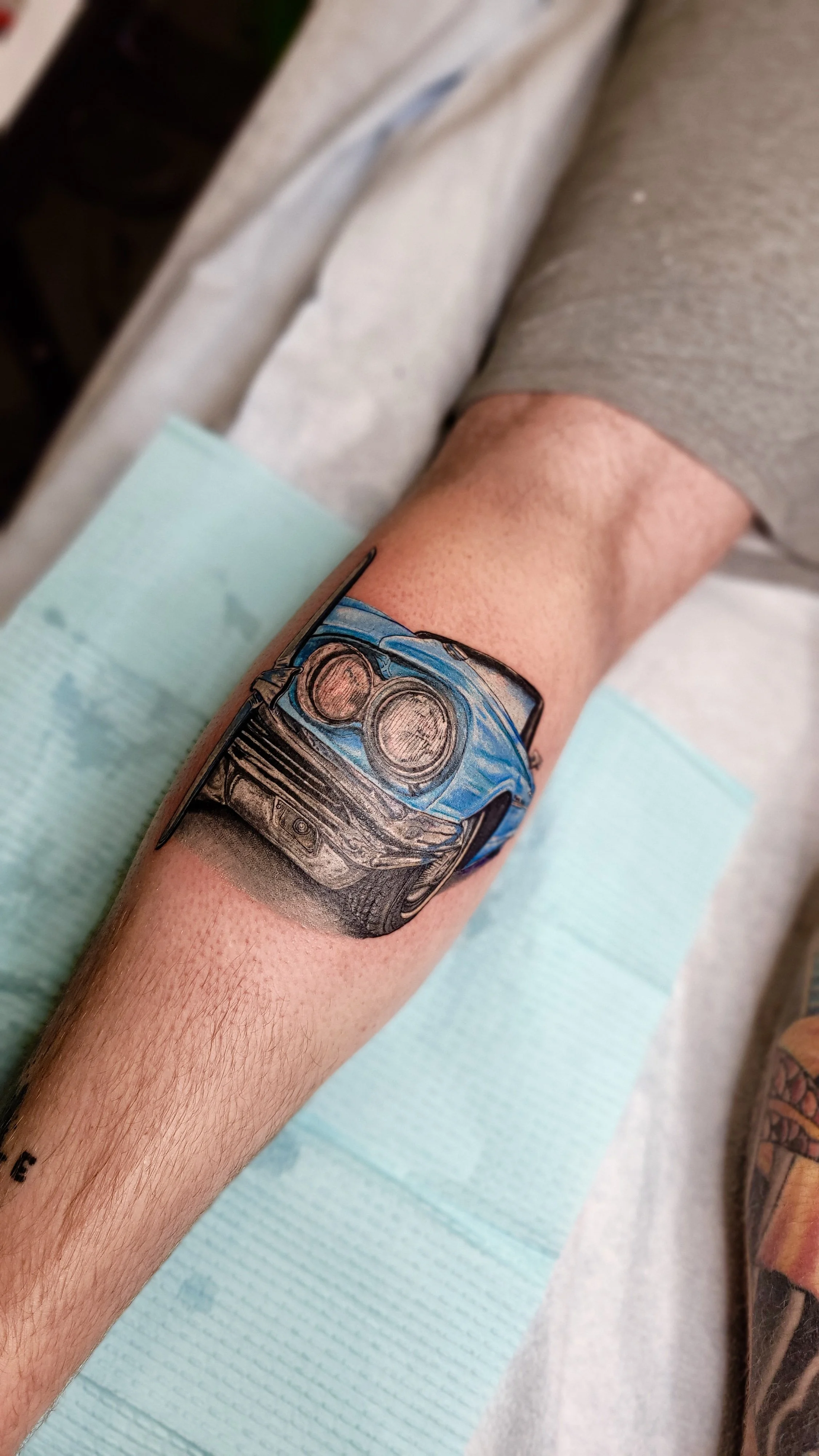 Tattoo of a blue sports car on a person's forearm.