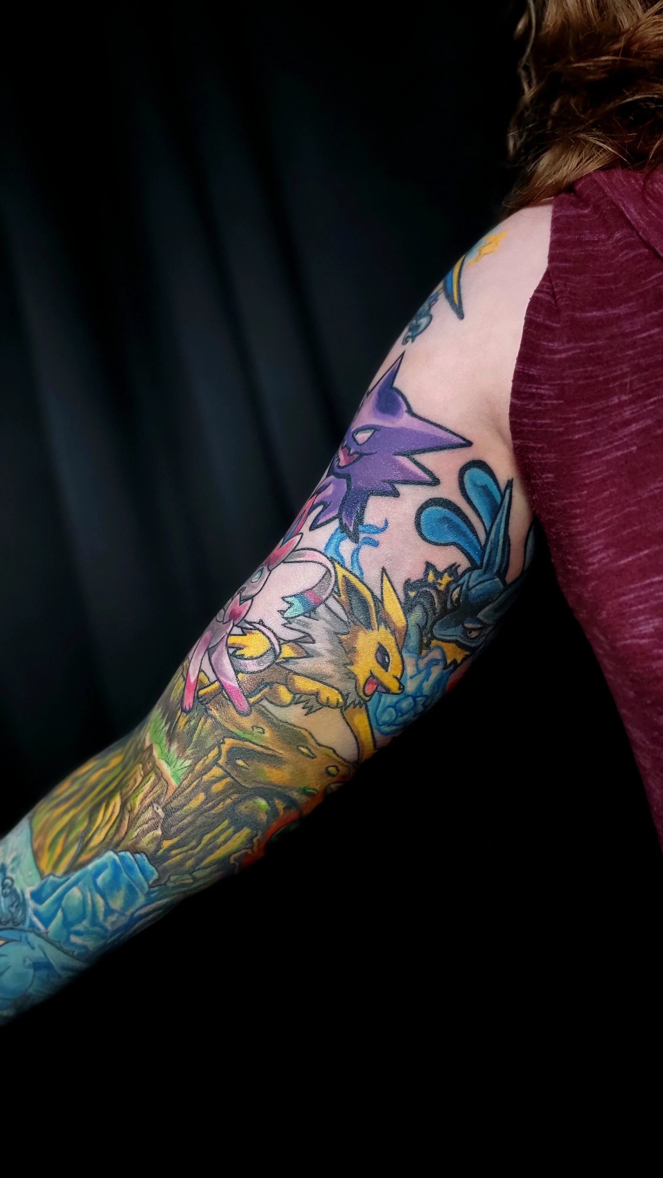 Close-up of a colorful tattoo sleeve featuring various Pokémon characters on a person's arm, wearing a maroon sleeveless shirt.