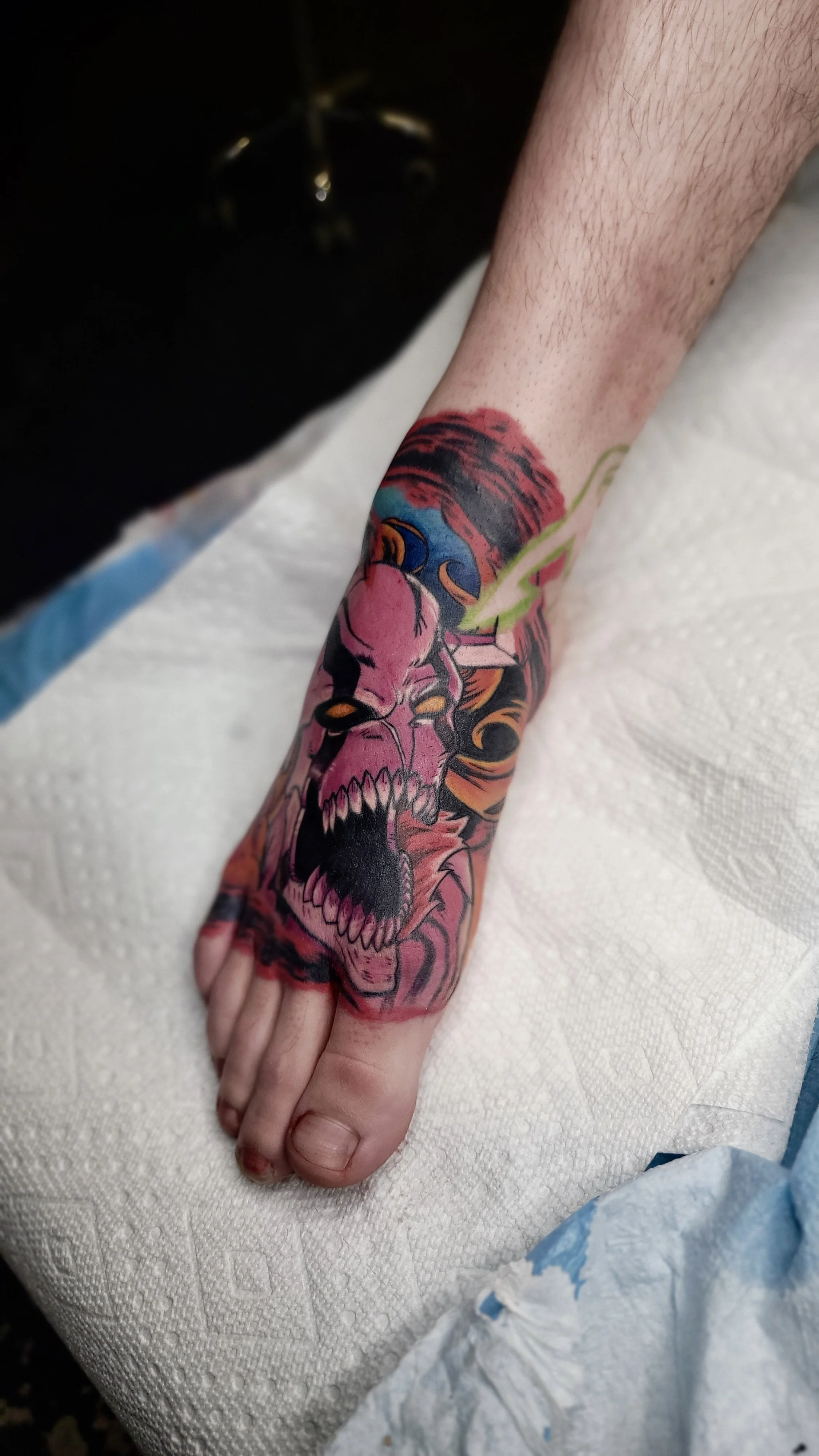 A person's forearm with a tattoo of a colorful, aggressive zombie face with its mouth wide open, showing sharp teeth, surrounded by abstract colors.