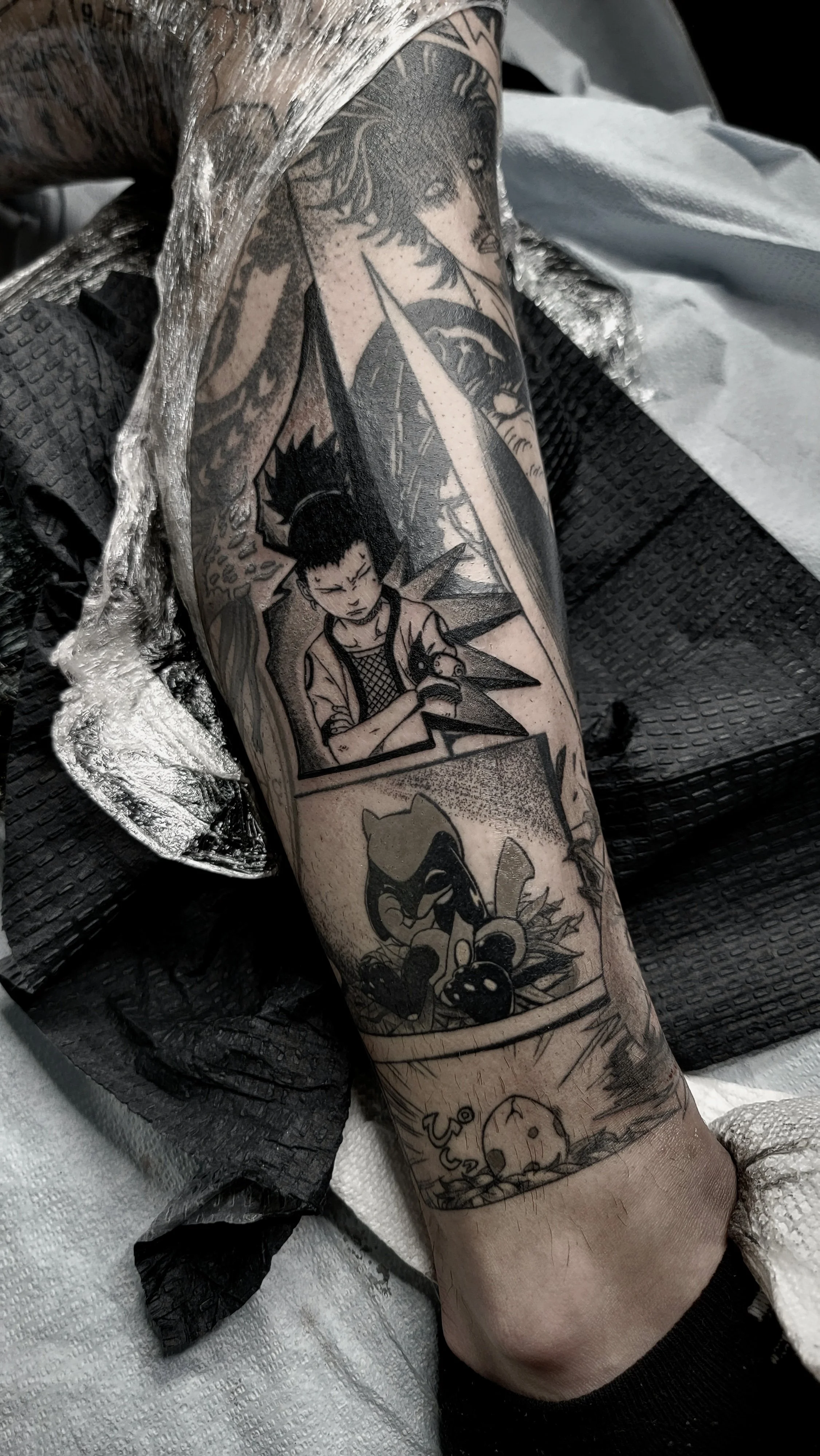 A tattoo sleeve on a person's arm featuring various black and gray comic-style characters, including a woman with flowing hair, a young man holding a Pokémon figure, and other cartoon elements.