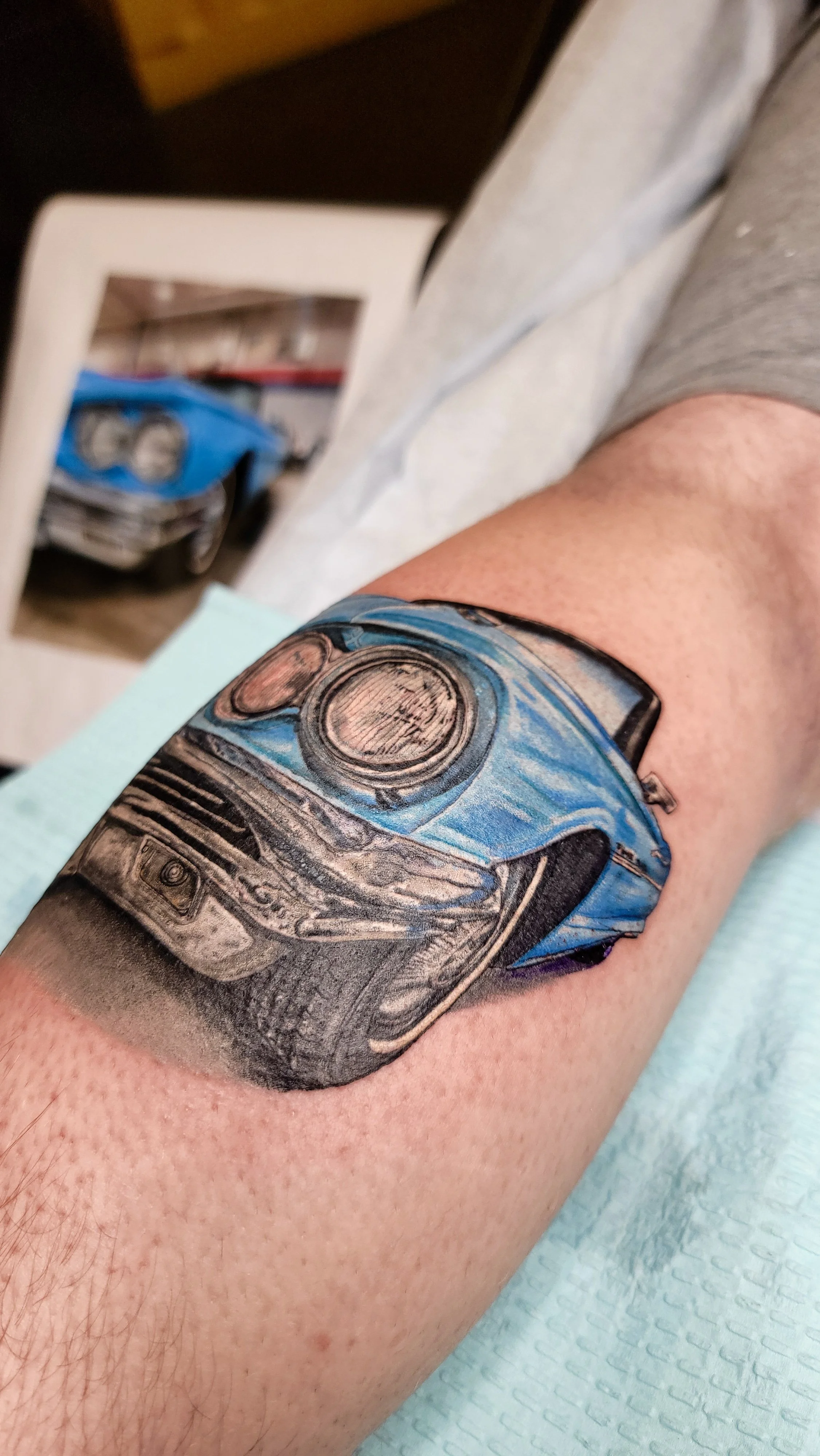 Tattoo of a blue sports car on person's arm near the elbow.