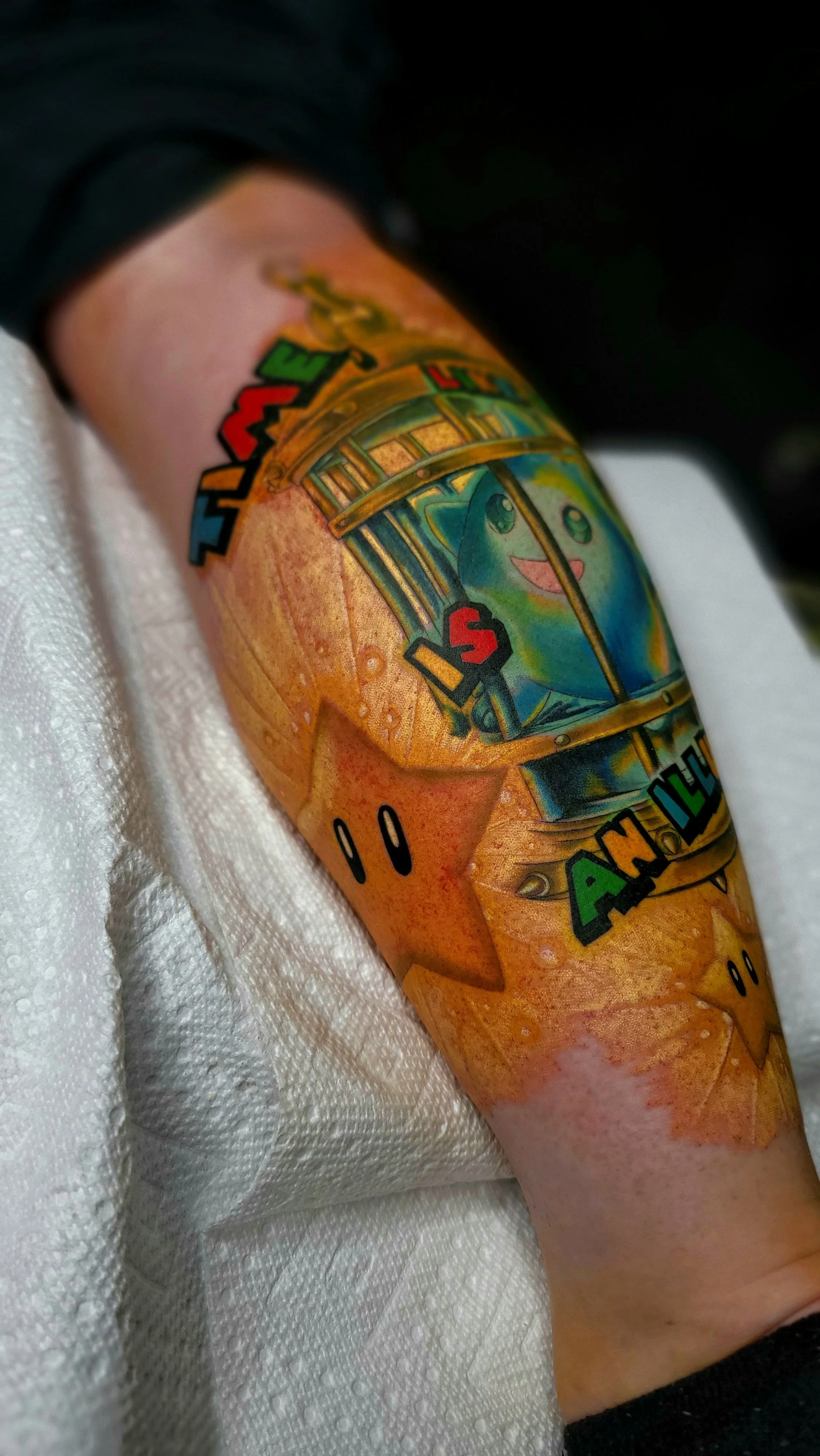 Tattoo of a train with a smiling face on a person's arm, with colorful letters spelling 'ANDER' and a black background.