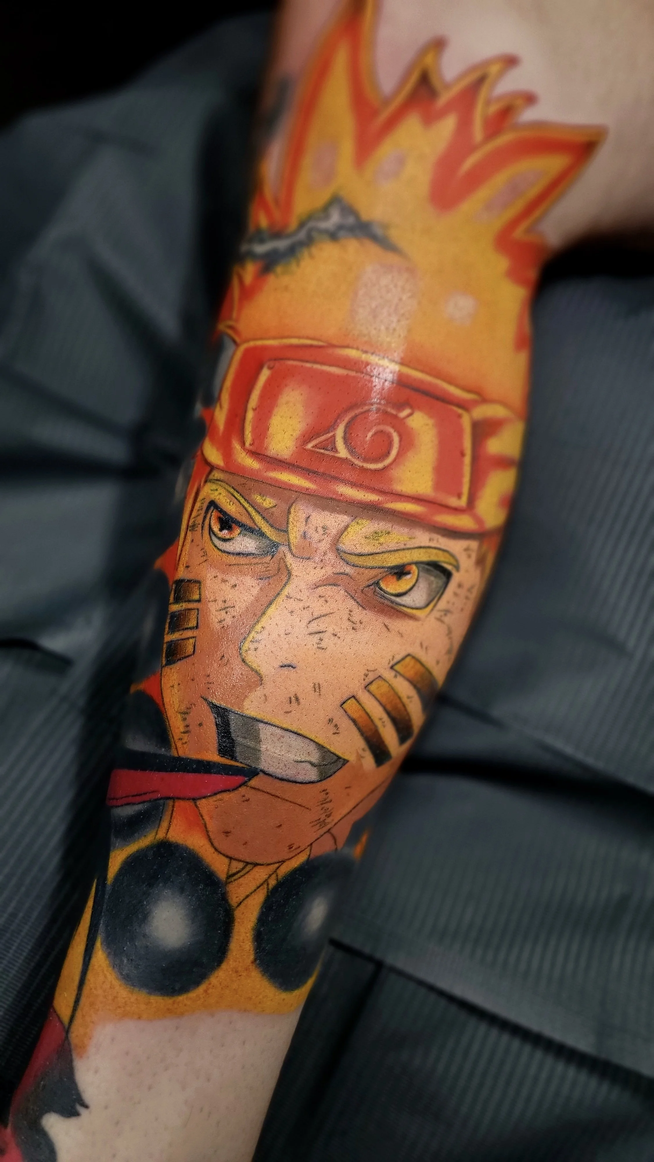 Close-up of a person's arm tattoo depicting Naruto Uzumaki, a character from the anime series, wearing his signature orange headband and headband with the leaf village symbol.