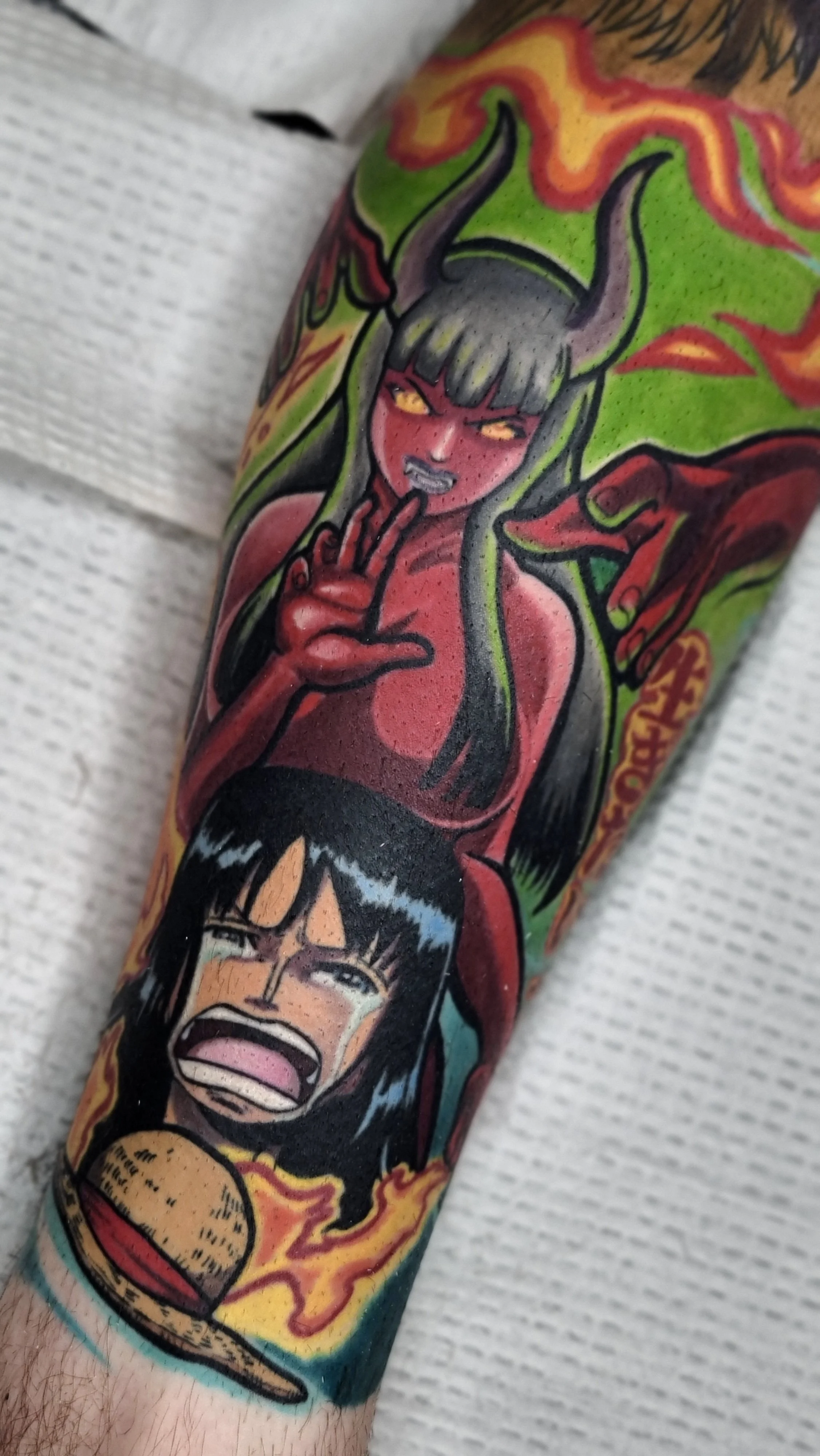 Tattoo of a woman with horns and yellow eyes making a shushing gesture, with a demon face and a face of a man with glasses, surrounded by flames on arm.