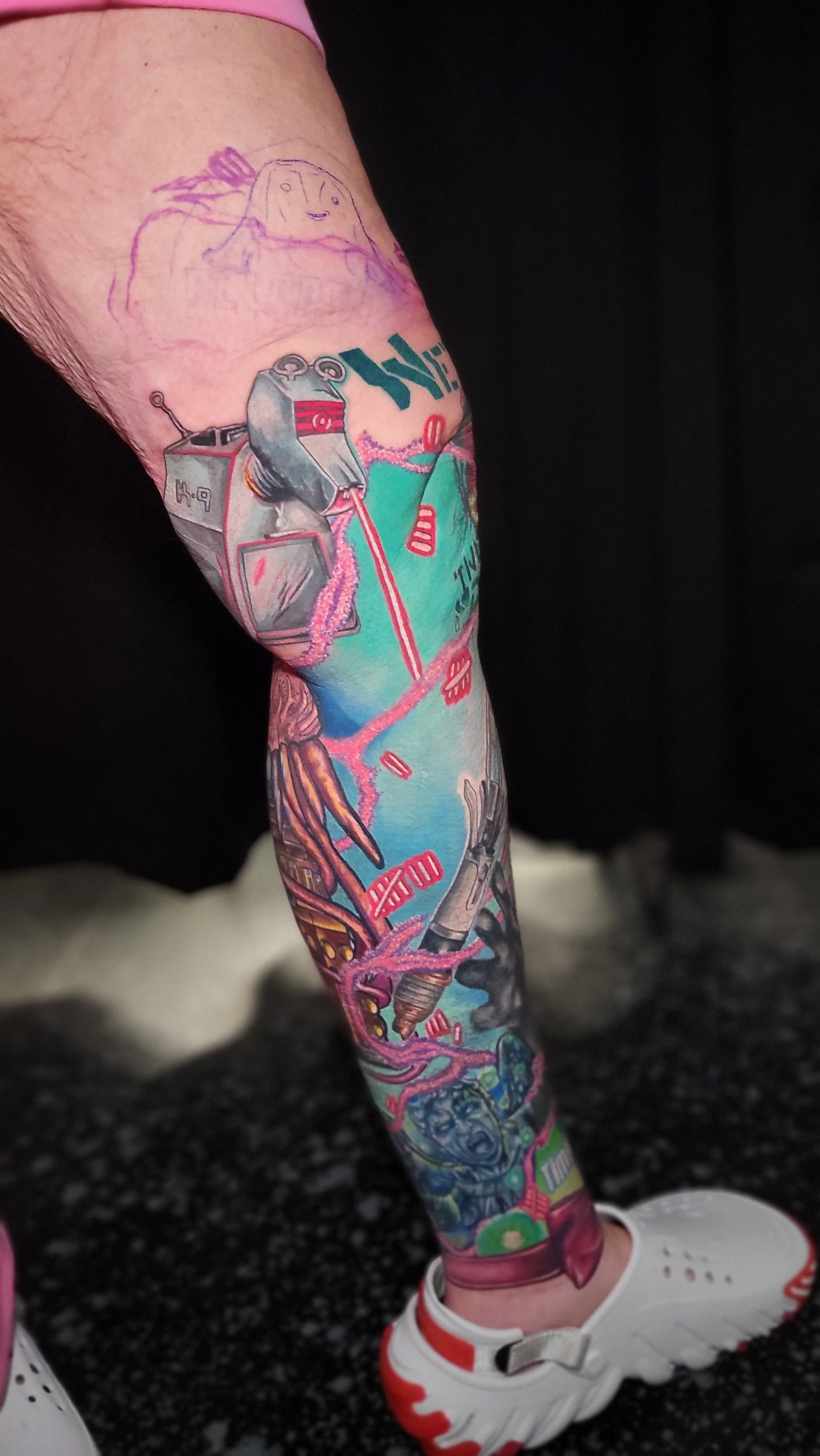 Colorful tattoo sleeve featuring various illustrations, including a robot, faces, and abstract waves on a person's leg, with white sneakers.