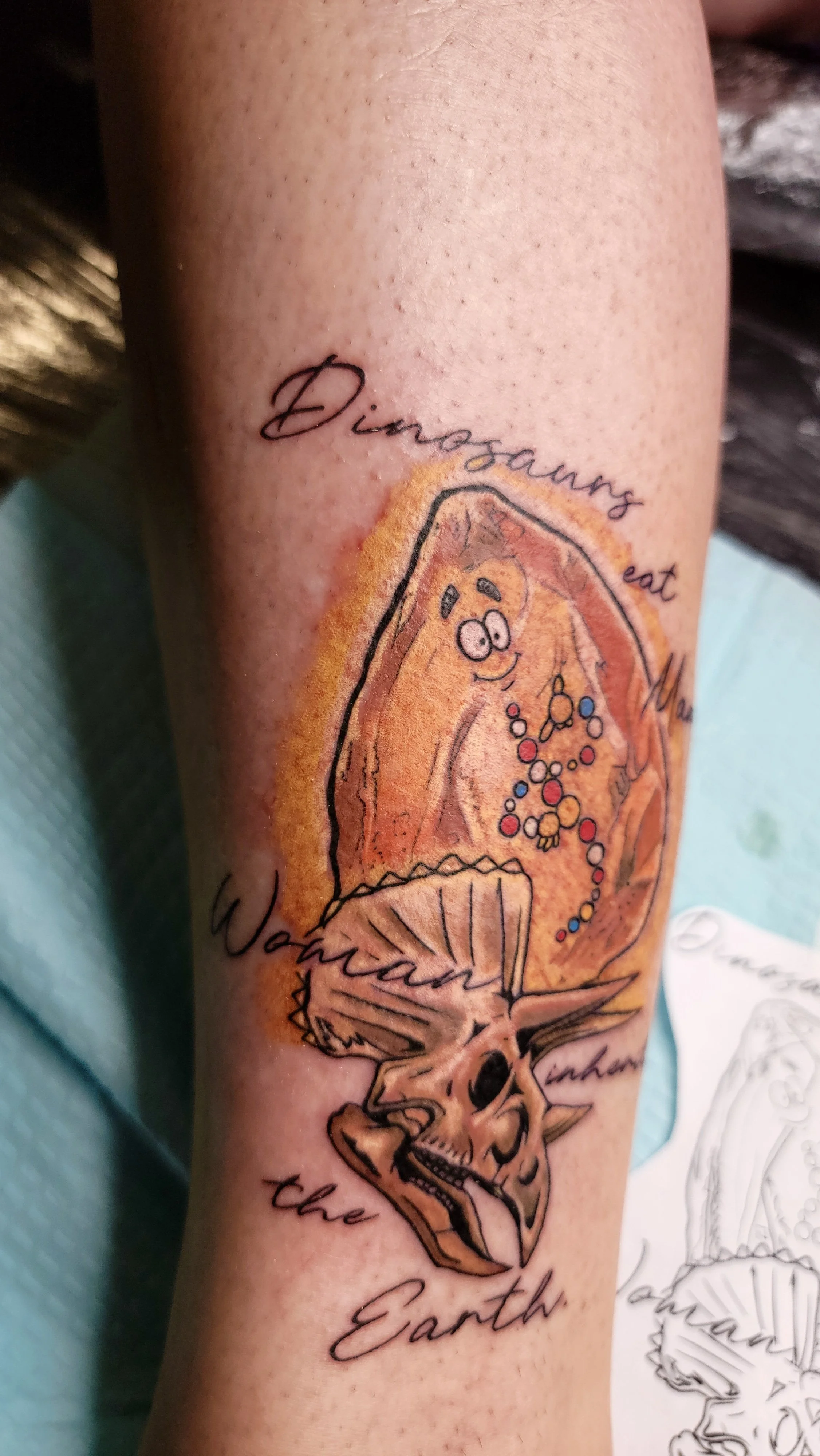 Tattoo on arm featuring a slice of pizza with a face, ice cream cone, and skeleton below it, with the words "Dreams eat" and "Earth" in script.