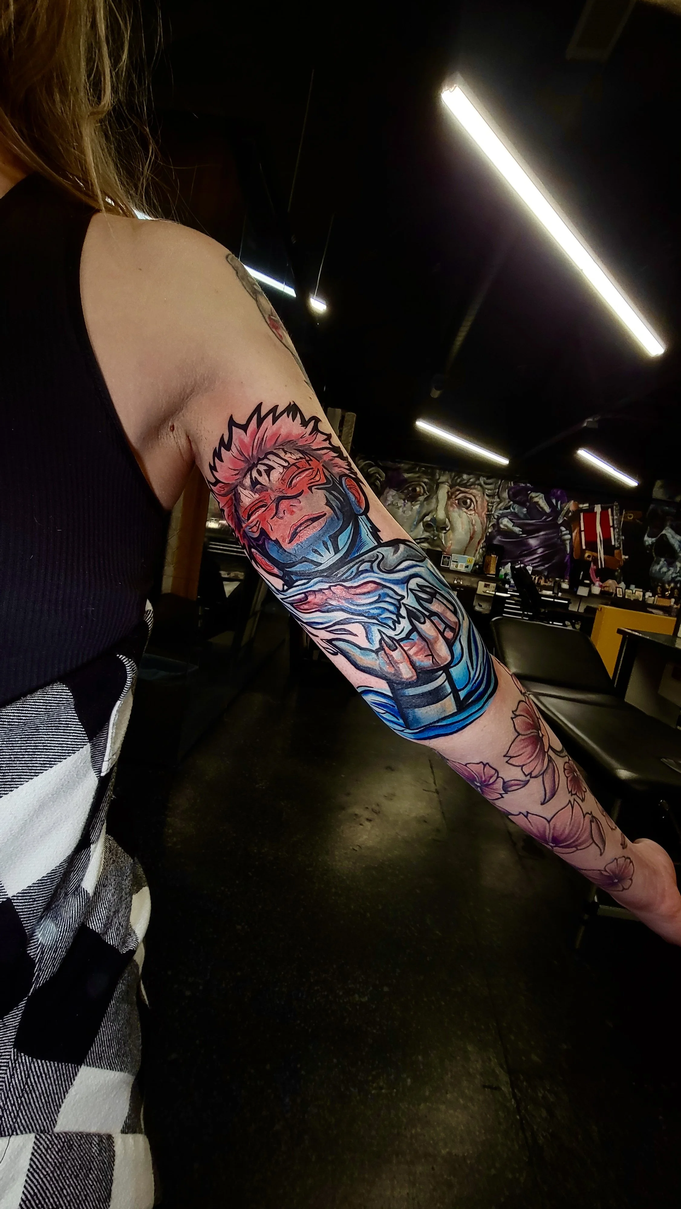 Colorful tattoo of a person's face with a vibrant background on the woman's upper arm in a tattoo studio.