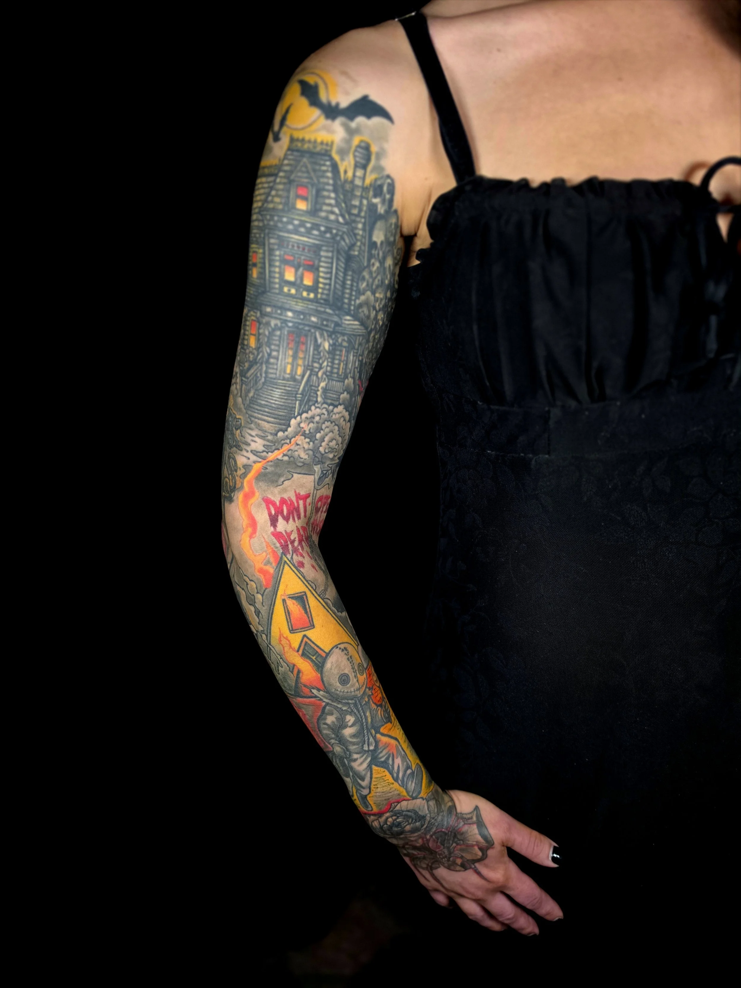 A person with a tattooed arm, wearing a black sleeveless top, against a black background.