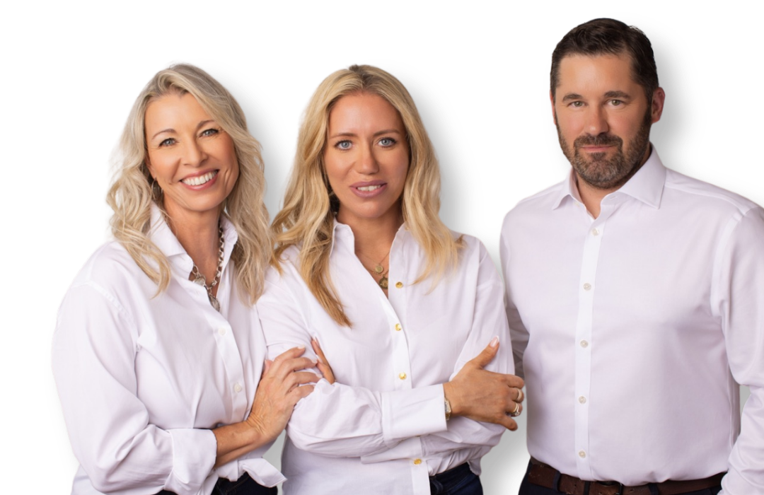 Three confident adults, two women and one man, standing close together in white shirts against a gray background.