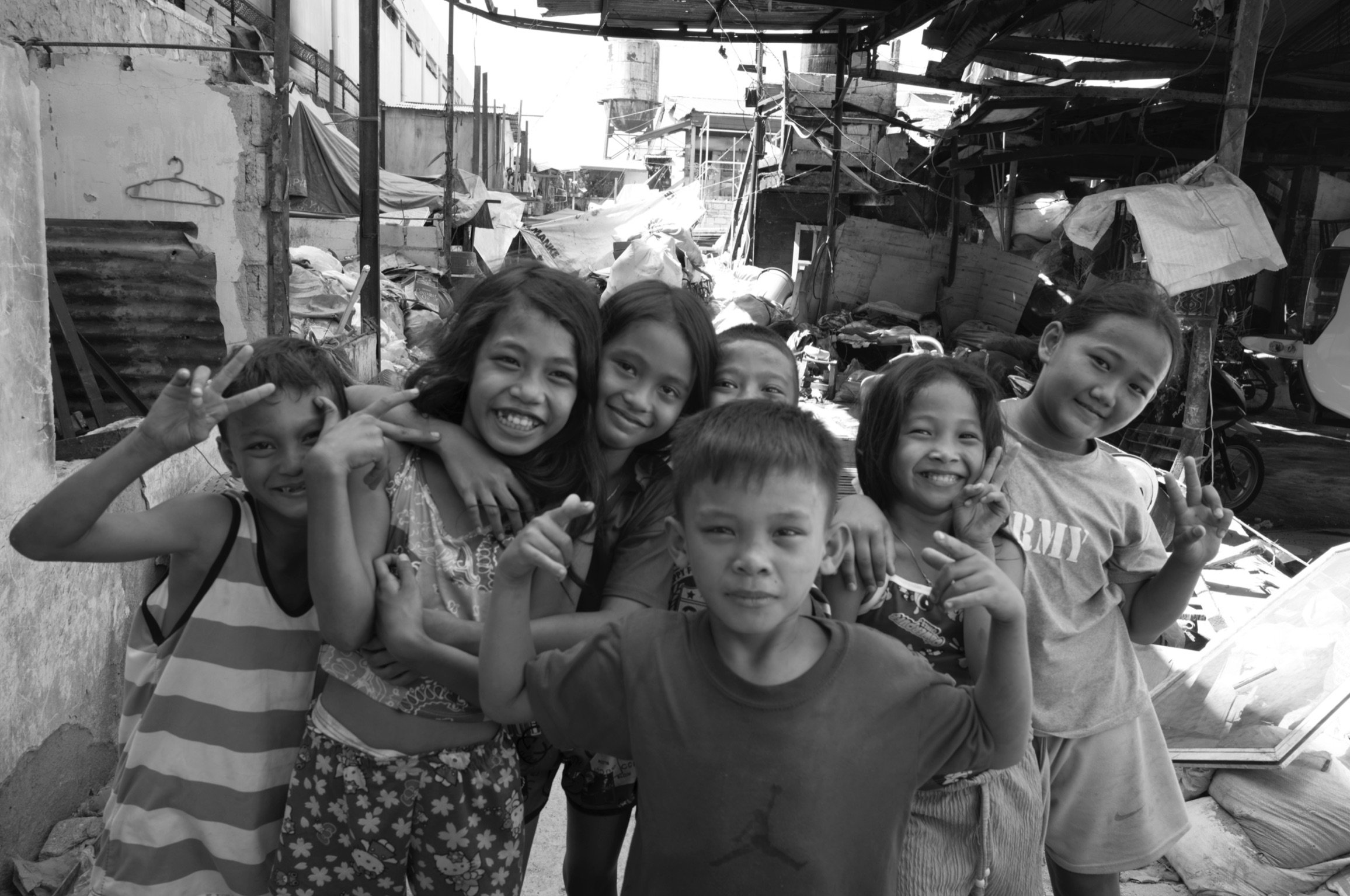 Group of children in a crowded, damaged urban area, smiling and making peace signs in Tondo, Manila ©R. Hartel for odoVita.
