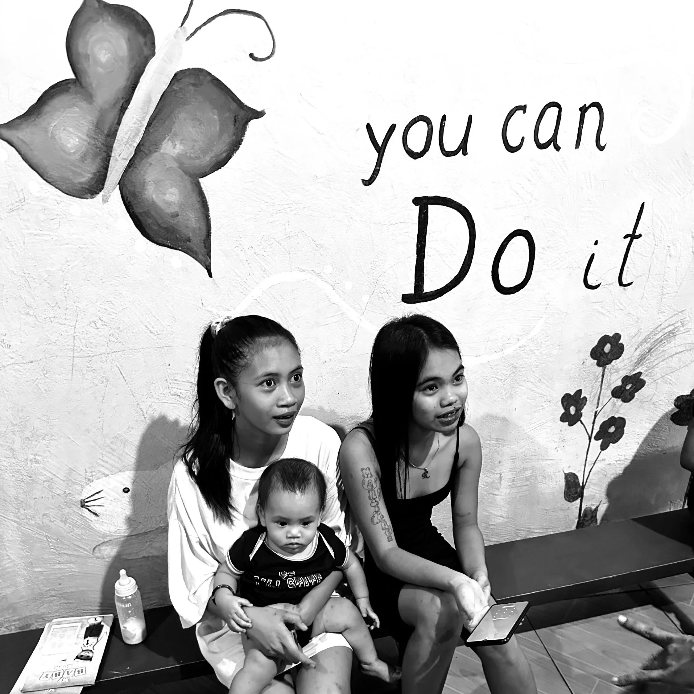 Group of children and a woman sitting together at a table, with flowers and a motivational sign that says 'you can do it' in the background.©odoVita