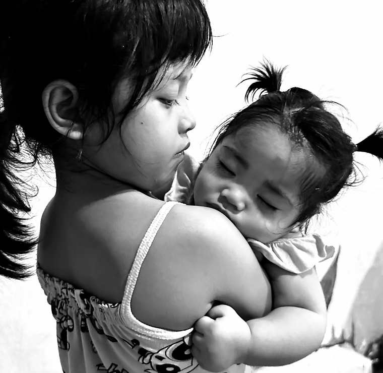 Two young girls hugging, one appears to be comforting the other, in a close embrace, black and white photo. ©odoVita