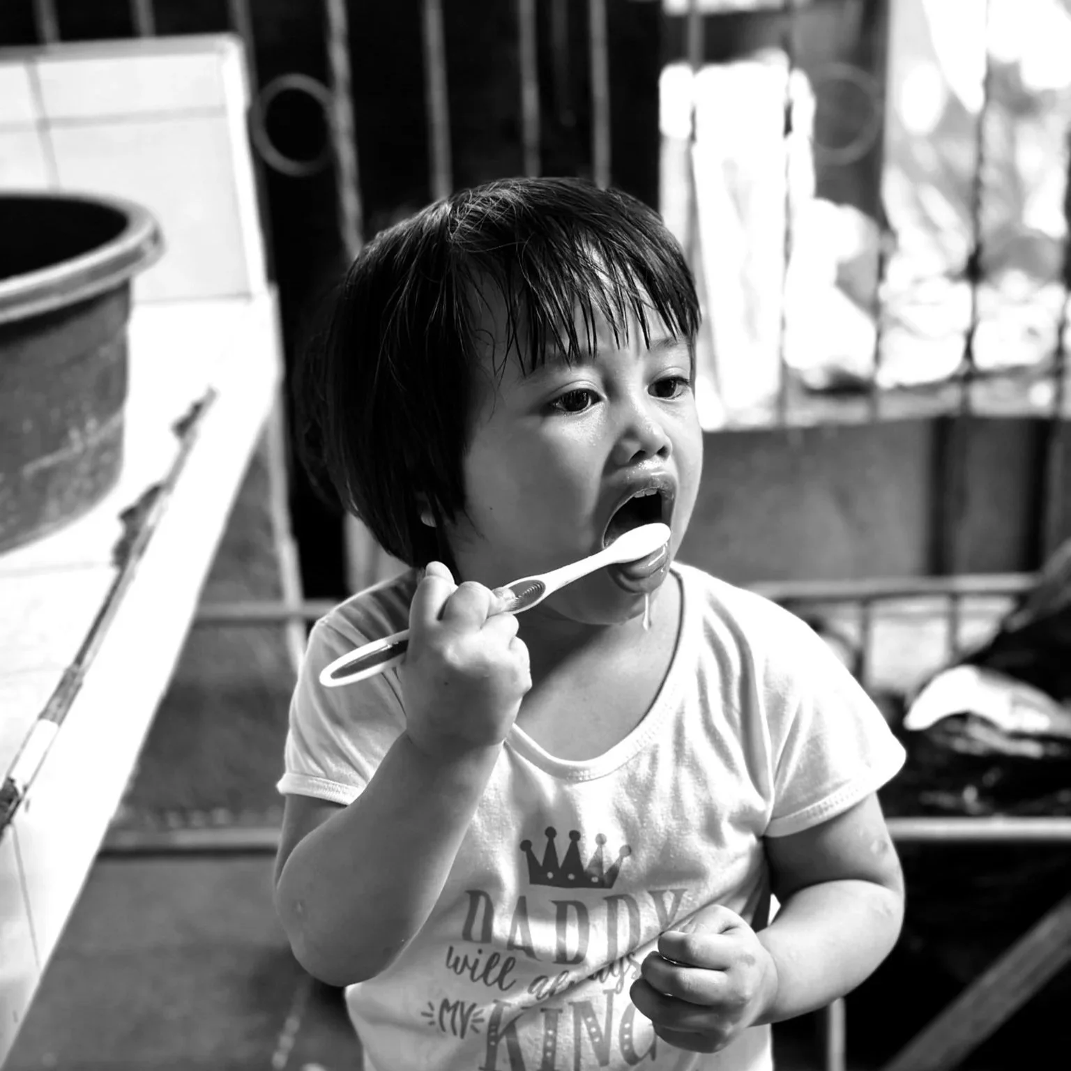 A young child with wet hair brushing their teeth with a toothbrush in a kitchen or laundry area.©odoVita