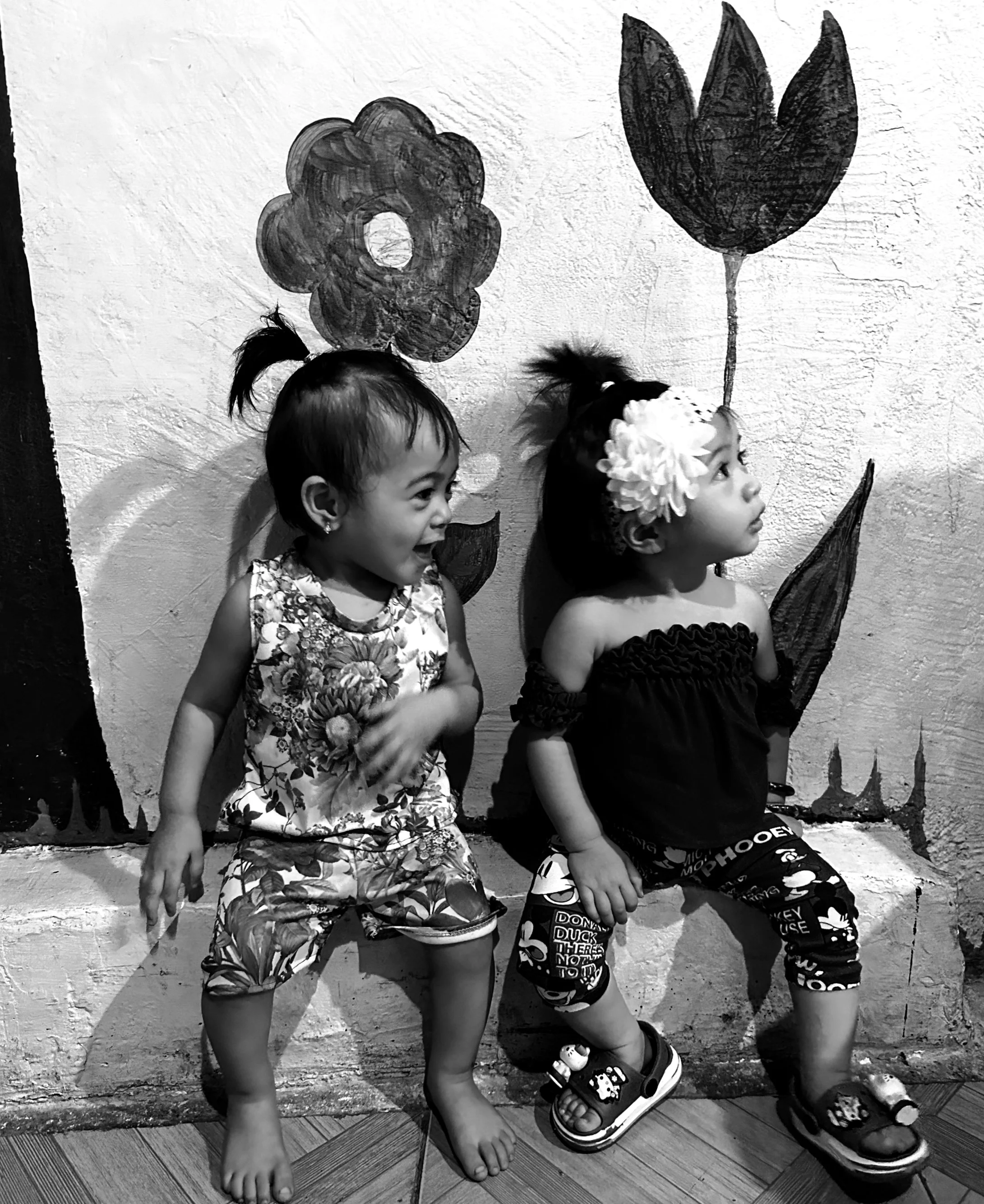 Two young girls standing side by side against a textured wall, both wearing shorts and sandals, with one girl smiling and the other looking to the side in Tondo, Manila ©odoVita.