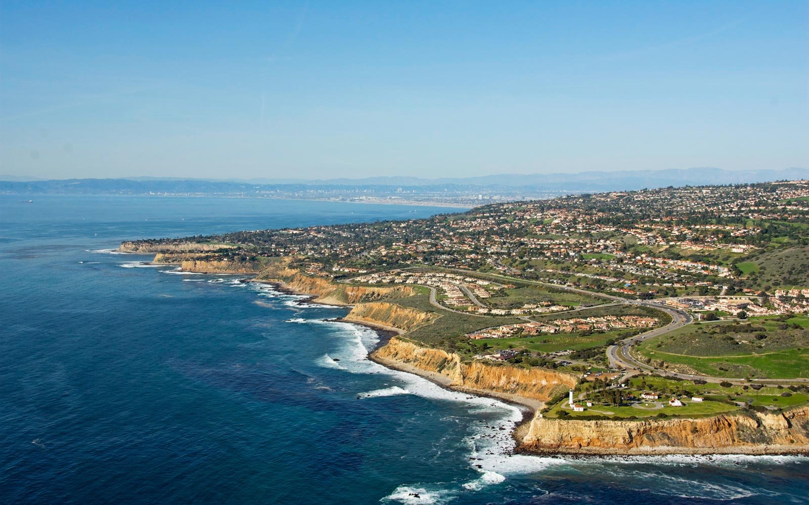 Aerial view of coastal cliffs with houses and a lighthouse overlooking the ocean in California.