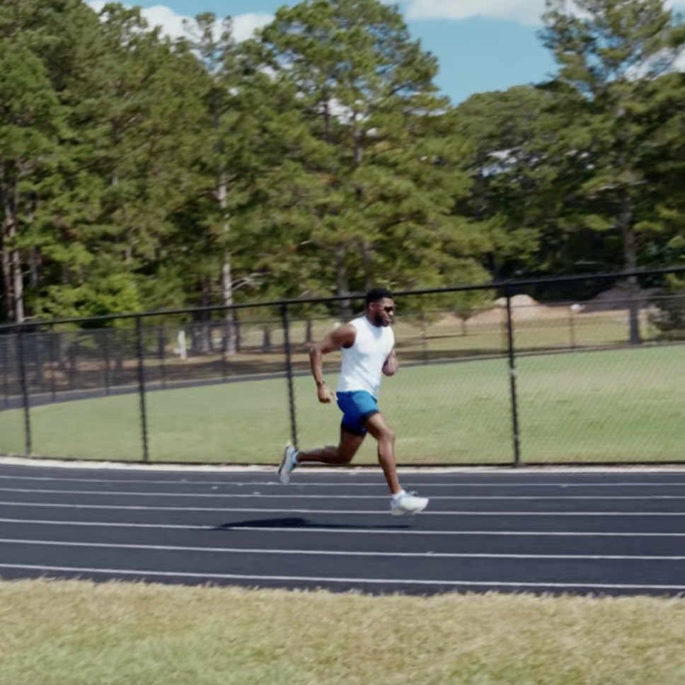 Man running on an outdoor track surrounded by green grass and trees.