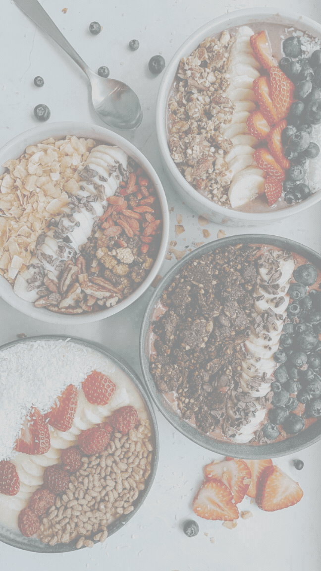 Four bowls of yogurt with granola and berries, on a light surface with scattered blueberries and a spoon.